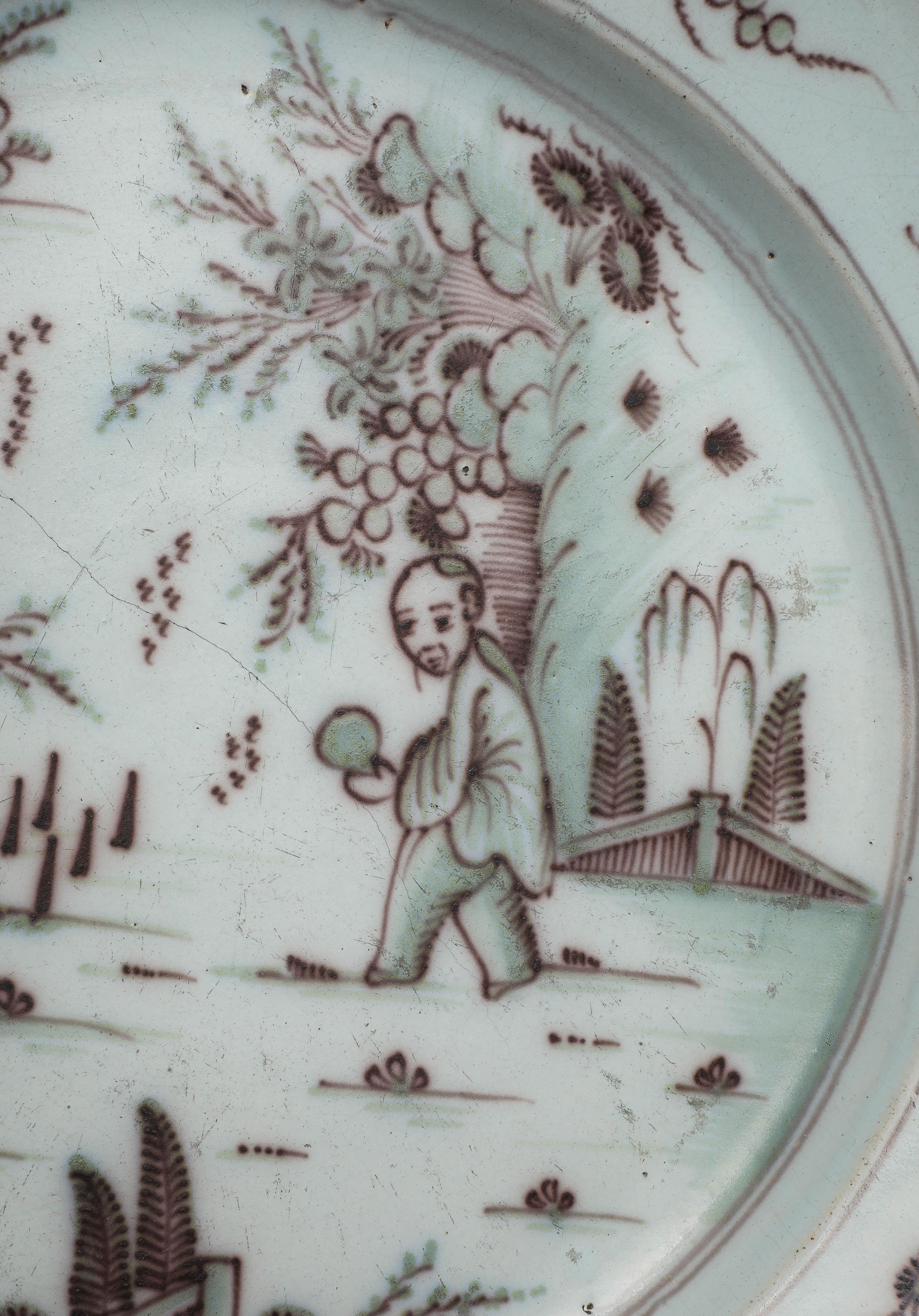 Early 18th century manganese tin glazed ceramic Delft charger. Hand-painted traditional chinoiserie scene featuring a figure within a garden landscape, green and brown paint. Hairline fracture down the center has been repaired. 