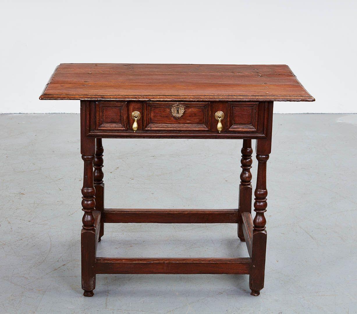An early 18th century English oak side table having molded edge three plank top with large overhang over single drawer with three molded panels having two brass drop pulls and central escutcheon, standing on baluster turned legs joined by a box