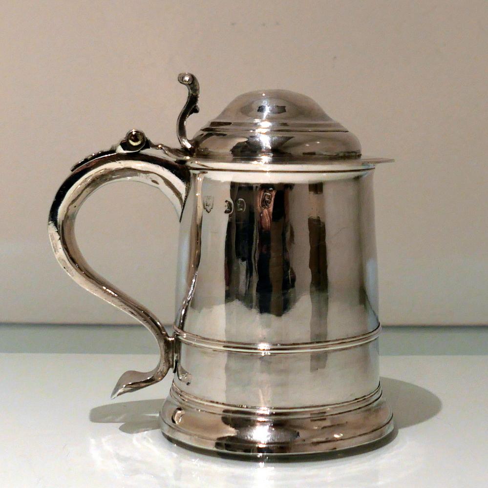 A rare and extremely collectable early Georgian silver cylindrical ‘ladies’ tankard and cover elegantly plain formed in design. The body tapers at the angles and sits on a ‘skirt’ foot. The hinged domed lid has an ornate cast thumbpiece and the