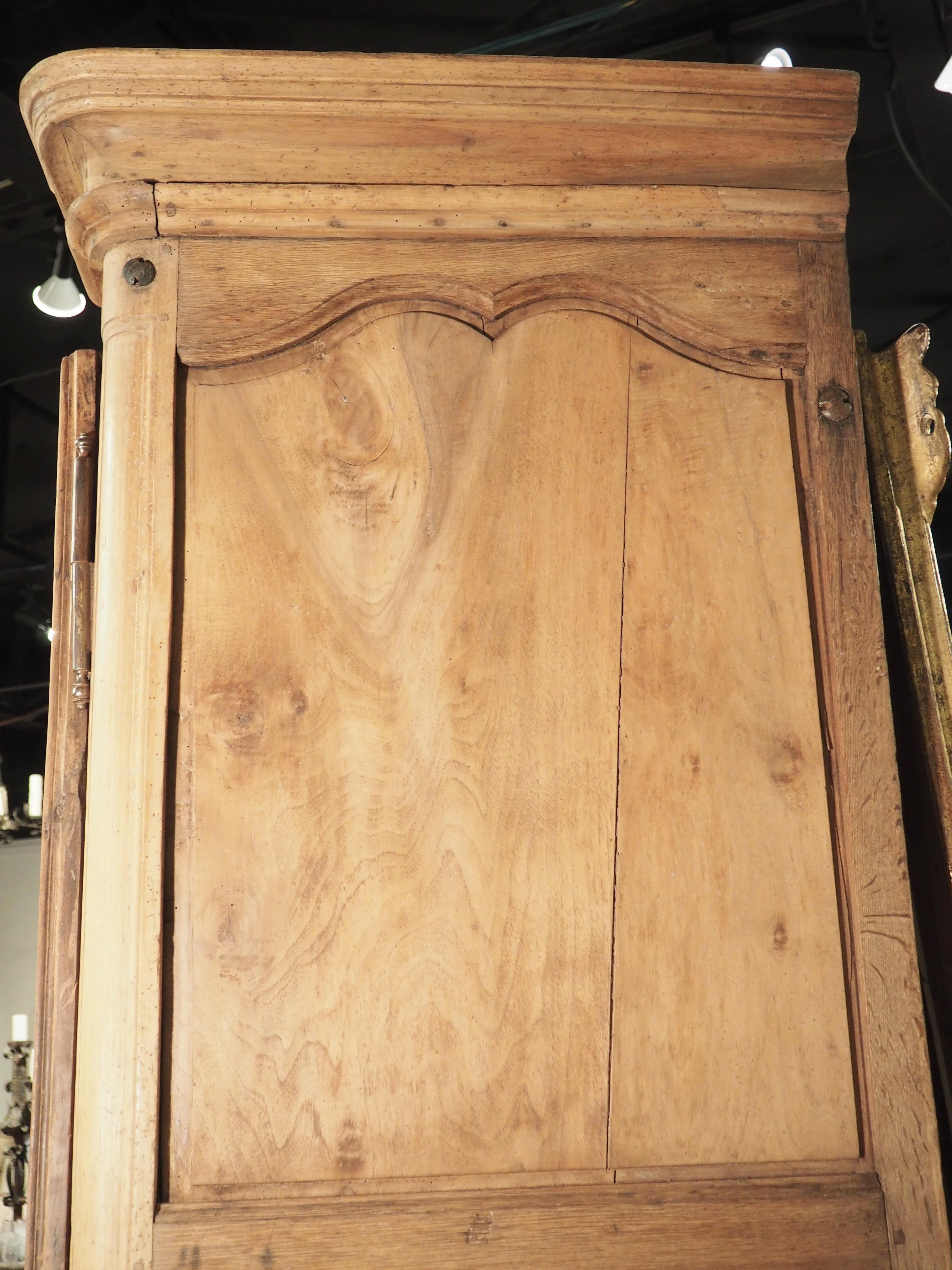 Typical of Ile-de-France furniture from the early 1700’s, this walnut armoire has unadorned panels, allowing the beautiful, curved moldings to take prominence. The walnut wood has been stripped of its original finish and bleached, leaving the wood a