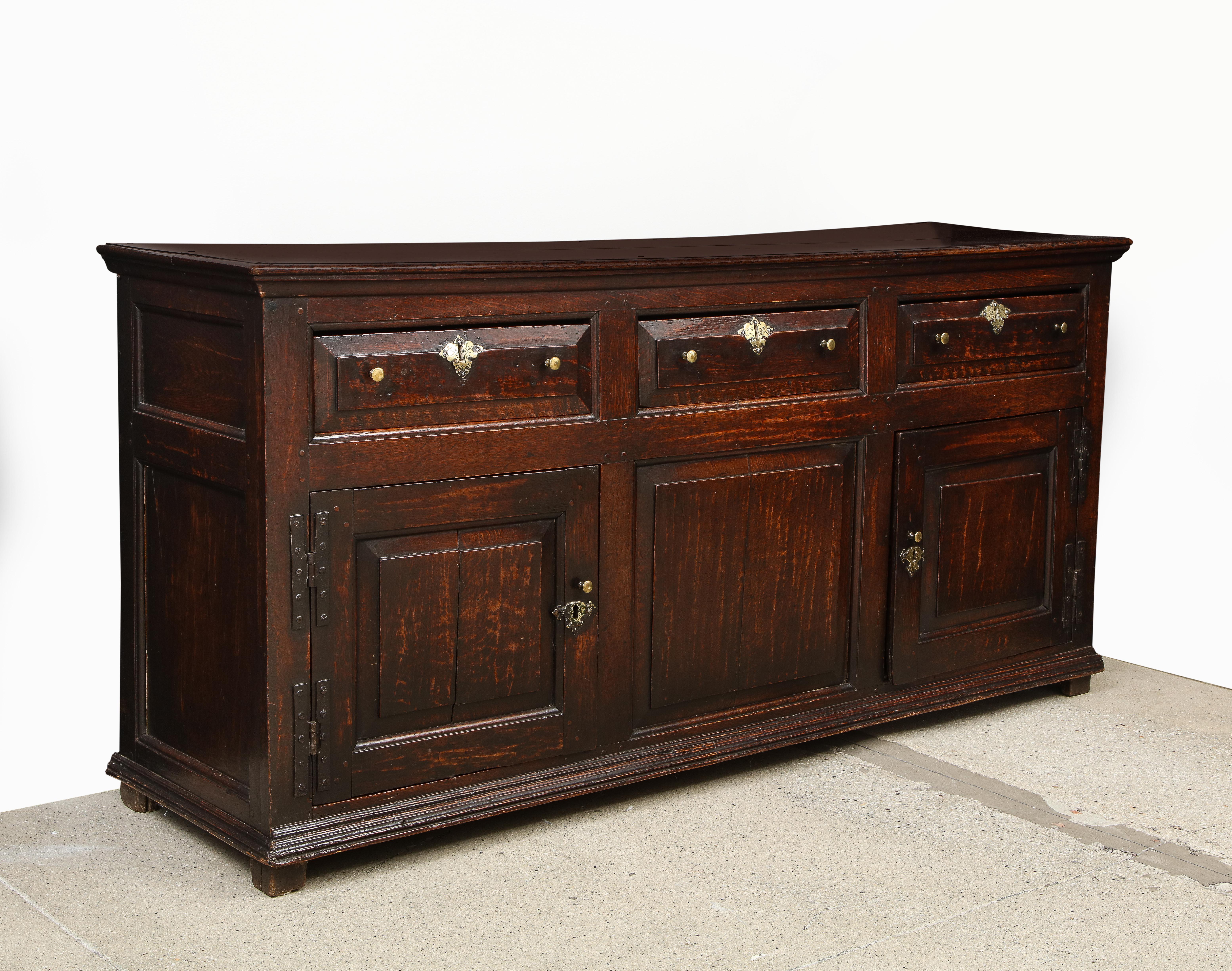 Very fine George I period oak low dresser, the molded top over three drawers with raised panel fronts over two raised panel doors flanking a fixed panel, with richly molded base and standing on original stile feet, rataining original brass pulls and