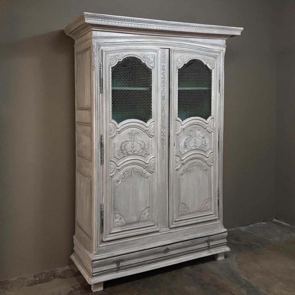 This Early 18th century, Country French, armoire bookcase features elaborately carved detailing and a wonderfully patinaed painted finish. Its stately 300 year elegance combines with it slightly rustic appeal to indicate the talented artisans who