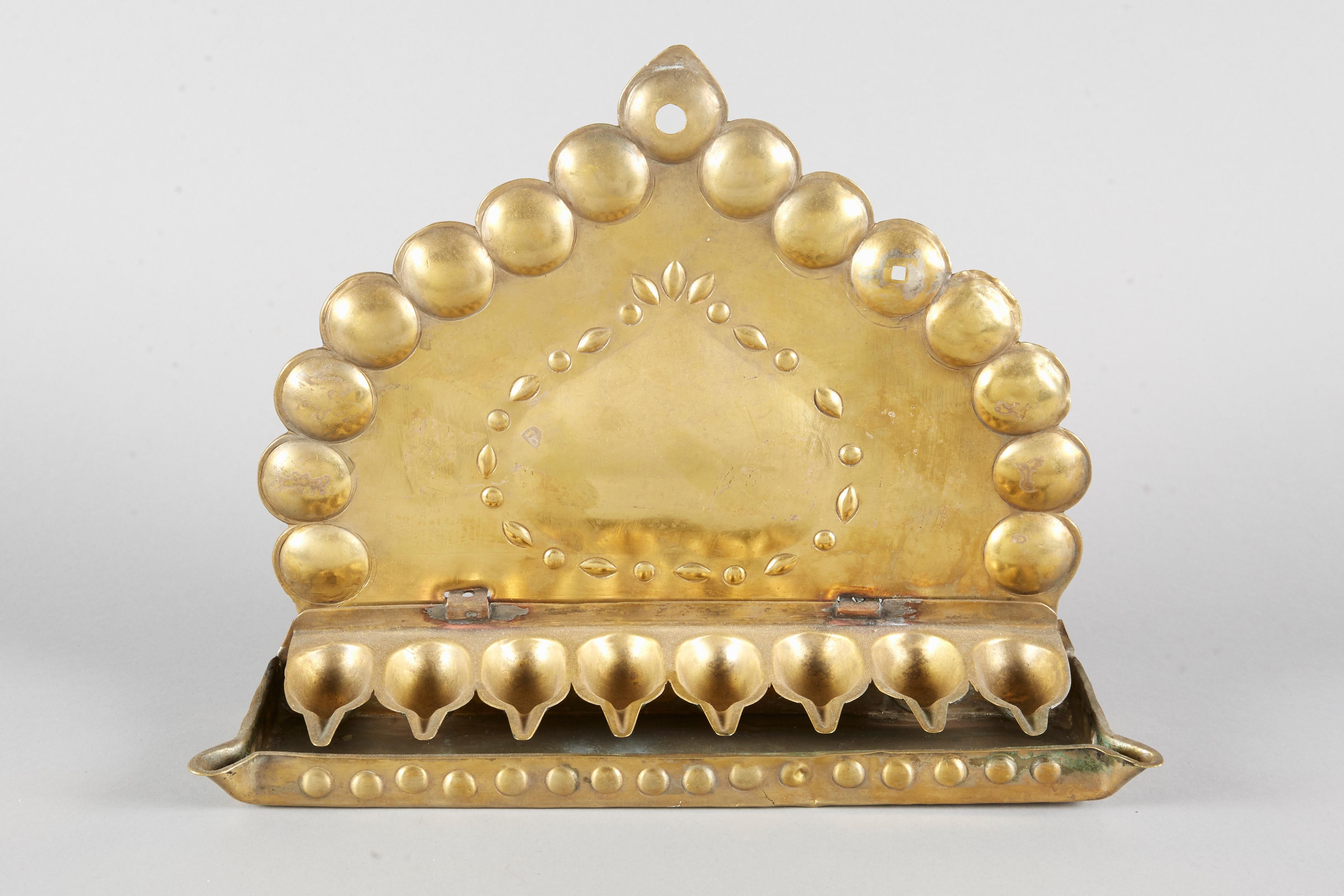 Cut, pierced, and repoussé brass sheet Hanukkah Lamp Menorah, The Netherlands, circa 1800. Backplate in the form of pointed arch, in its center a convex in the form of an upside-down heart surrendered by leaves and circles, on the plate margins are