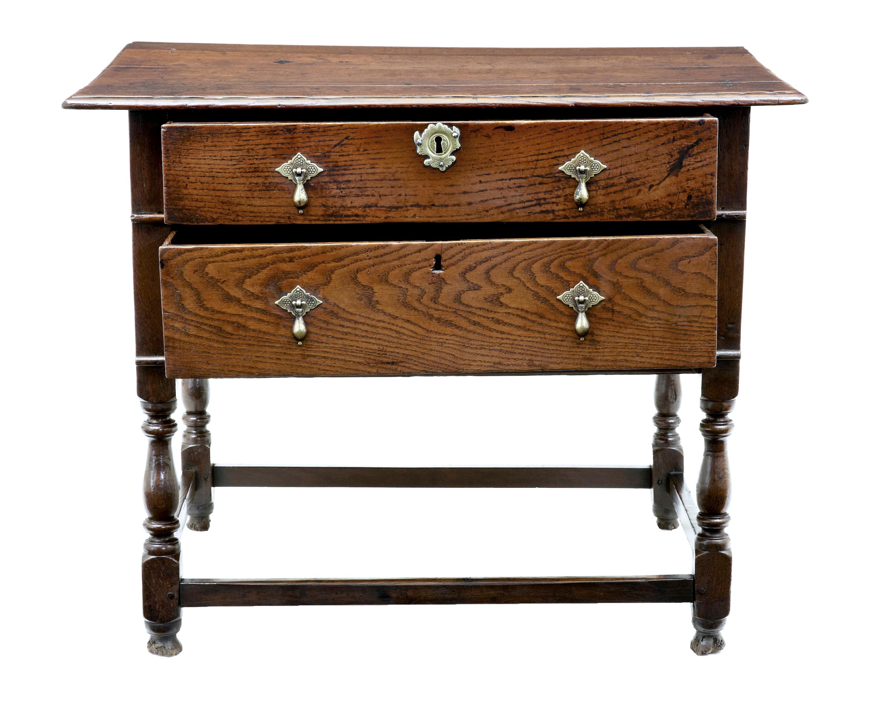 Very rare early 18th century two drawer oak side table, circa 1730.

Over-sailing 4 plank oak top, with 2 deep drawers below, fitted with ornate brass droplet handles and escutheons. Standing on 4 turned legs united by stretcher.

Great color