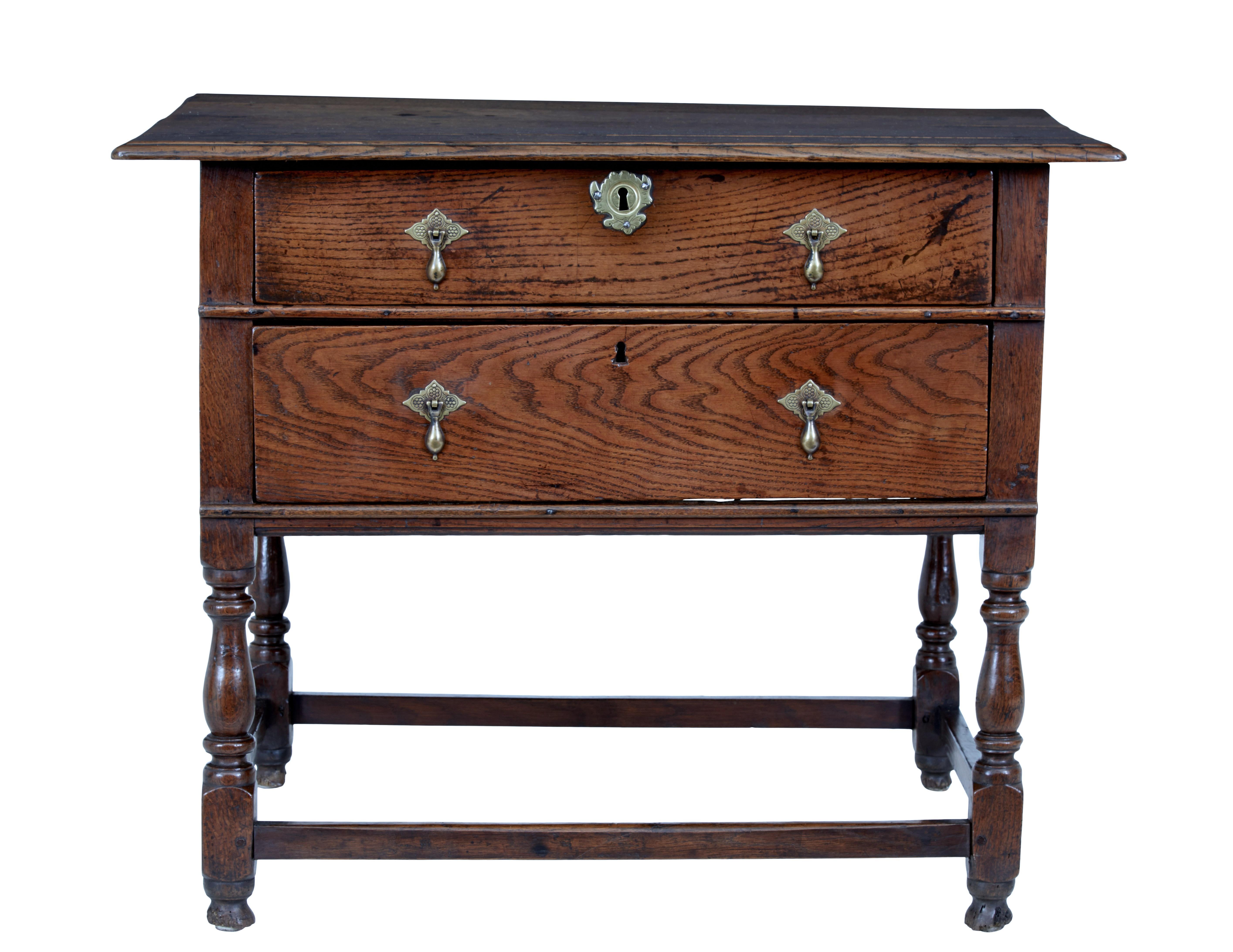 Very rare early 18th century two drawer oak side table, circa 1730.

Over-sailing 4 plank oak top, with 2 deep drawers below, fitted with ornate brass droplet handles and escutheons. Standing on 4 turned legs united by stretcher.

Great colour