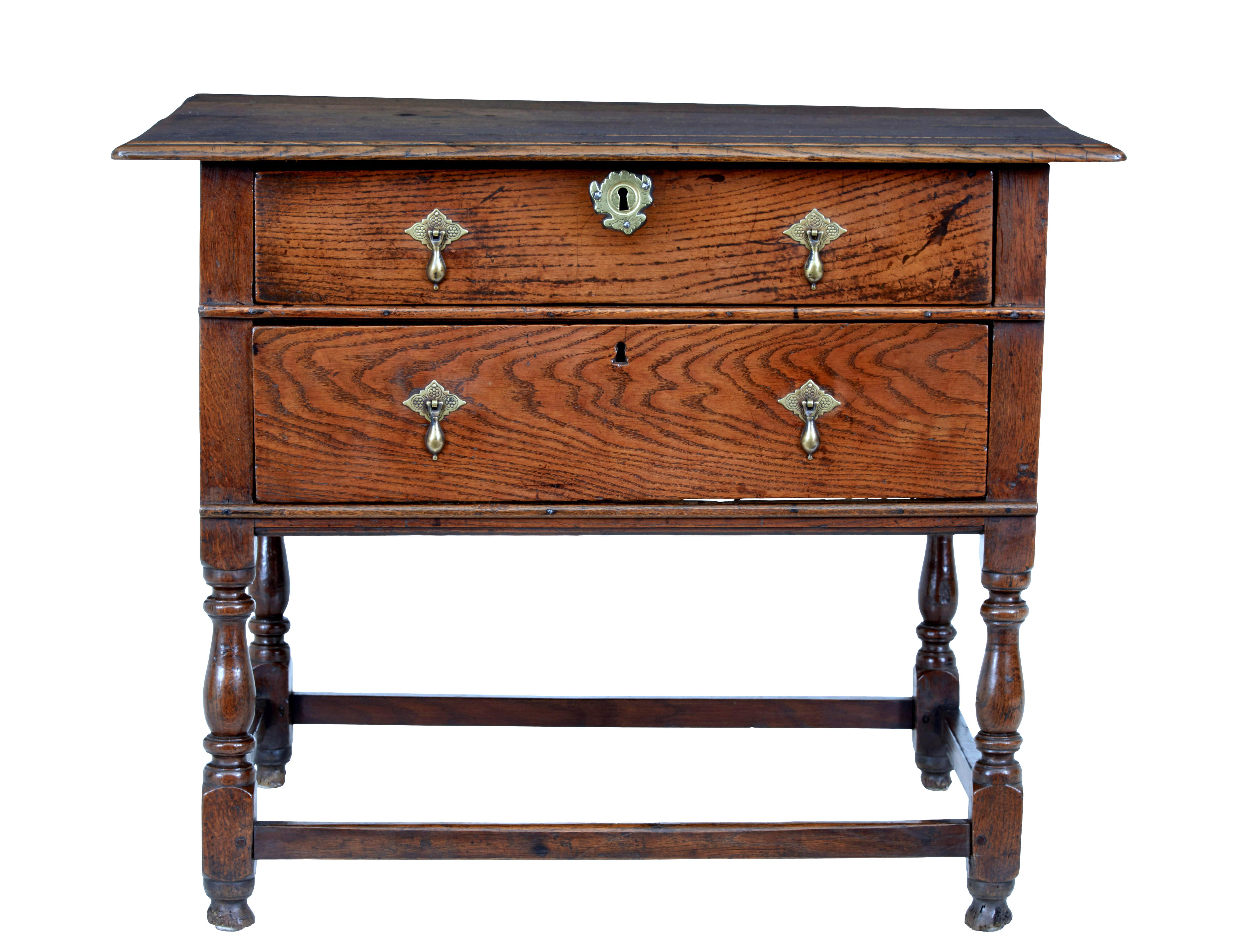 Very rare early 18th century two drawer oak side table, circa 1730.

Over-sailing 4 plank oak top, with 2 deep drawers below, fitted with ornate brass droplet handles and escutheons. Standing on 4 turned legs united by stretcher.

Great color and