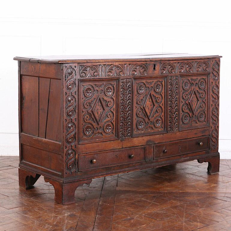 Large early 18th century carved oak coffer, the three-panel front with ornately-carved details. Lower drawers just a facade; drawers themselves no longer present. Standing on bracket feet. 

