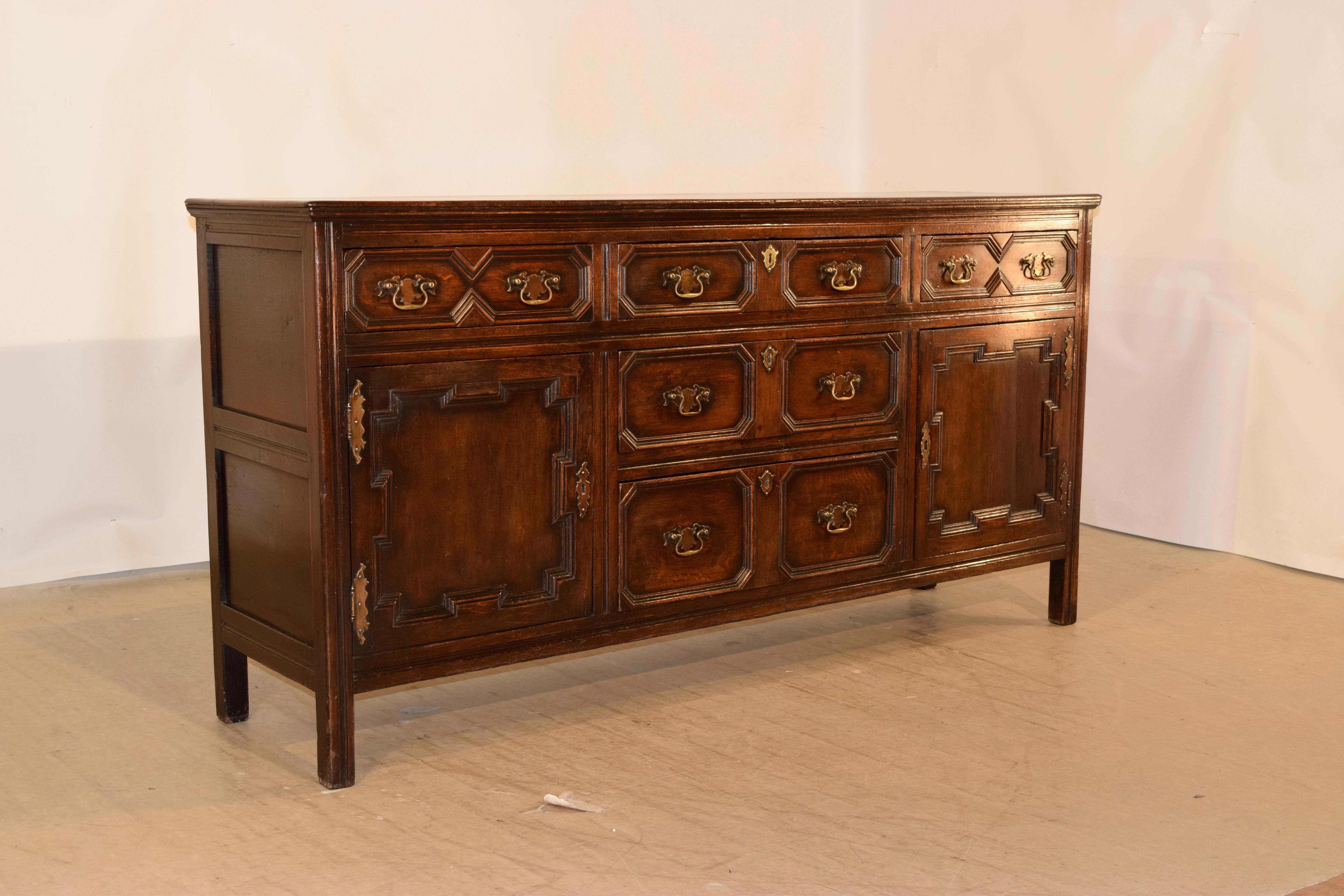 Circa 1720 English oak dresser base with a beveled edge around the top following down to paneled sides. The case has three geometrically paneled drawers over two central geometrically paneled drawers, which are flanked by geometrically raised