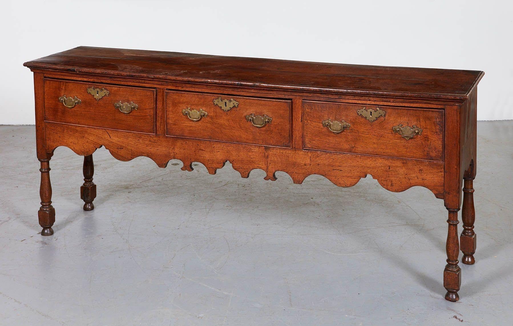 Good English oak low dresser, having molded top over three drawers over scalloped apron and standing on bold turned legs ending in original ball feet and with pleasing nutty color.