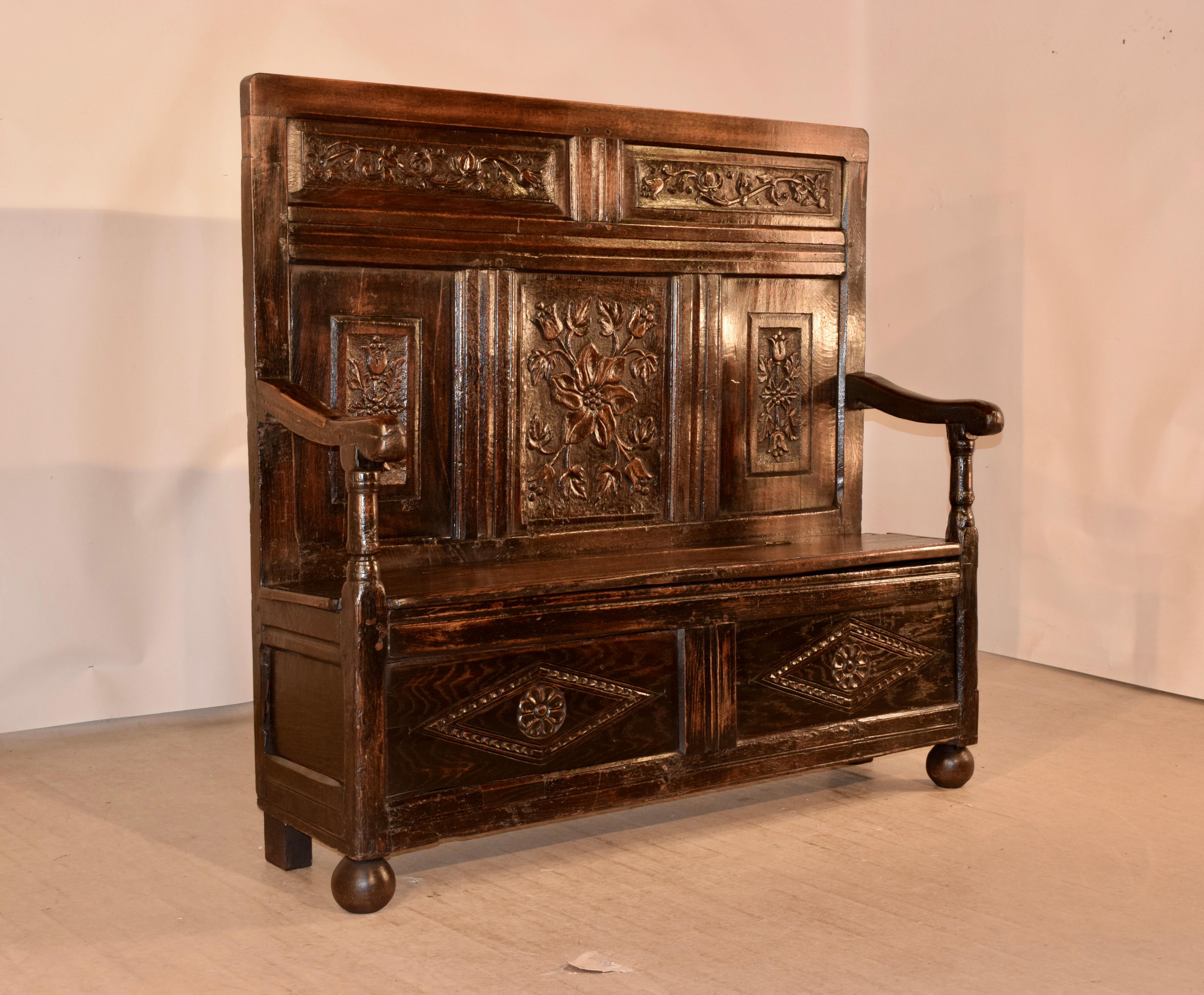 Early 18th century oak settle from England with a paneled back which has hand carved floral decorations in each panel. The seat measures 19.5 inches in height and lifts to reveal storage. The base is paneled on the sides and front, and the front