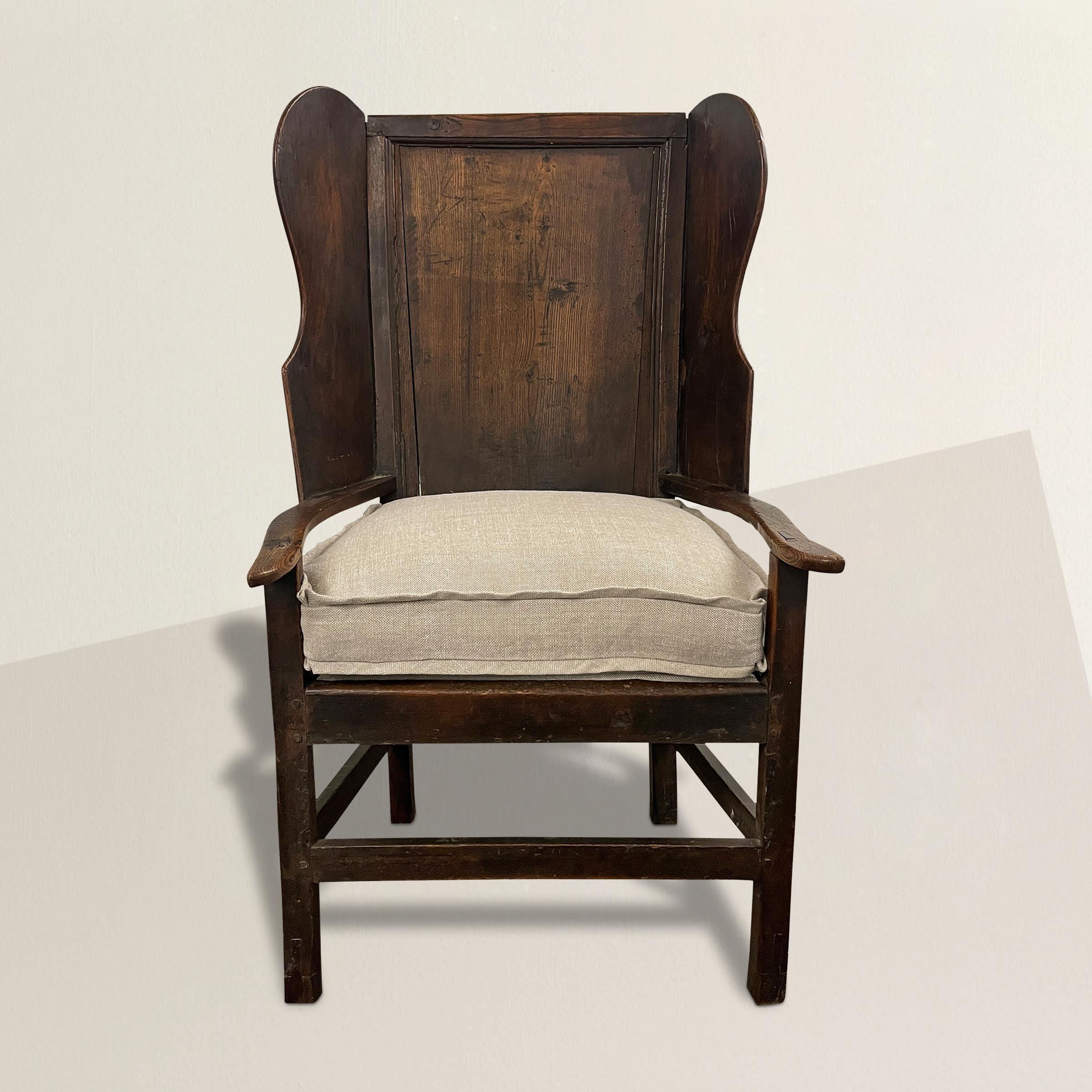 A remarkable early 18th century English oak wingchair of simple form and construction with applied wings to a gently sloping paneled back, slightly out turned arms, and newly upholstered with a down-filled Belgian linen cushion with a double flange.