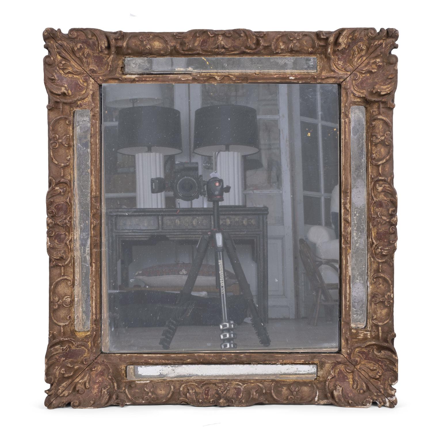 Early 18th century French giltwood mirror in Regence style, circa 1730-1750. Marginal mirror plates border a larger central mirror plate on all sides set within embellished giltwood moldings. The frame is carved with strapwork, foliage and flowers,