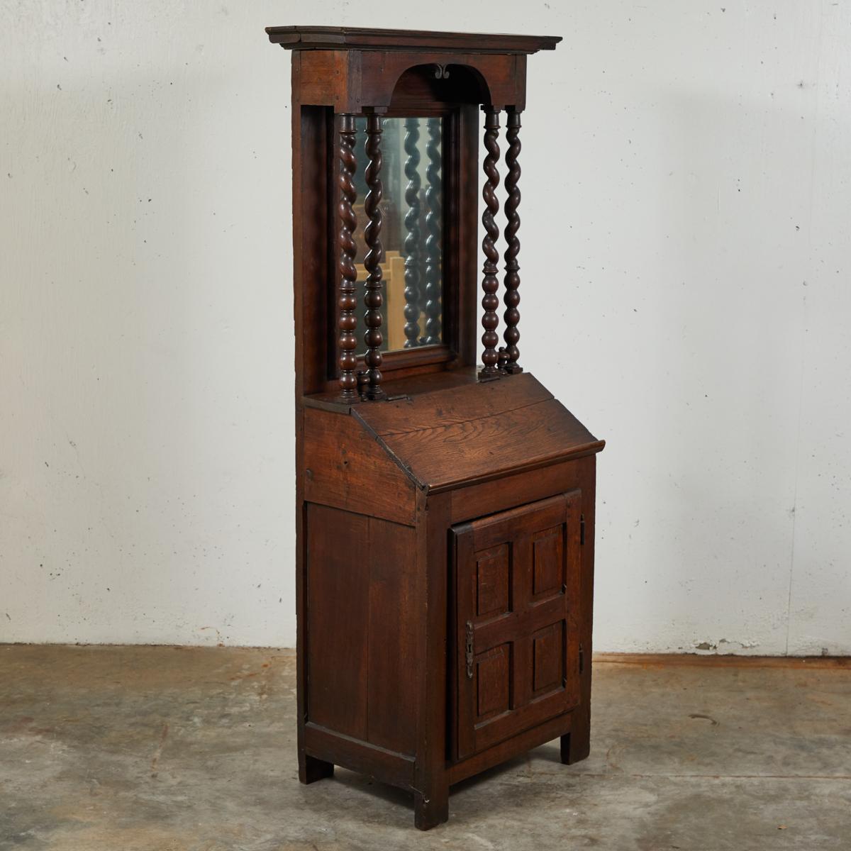 Early 18th-century French dark wood secretary or fall-front bureau cabinet with charming proportions. Featuring a carved projecting cornice and arched front, original glass mirror fronted by barley twist columns, and slant front desk with a