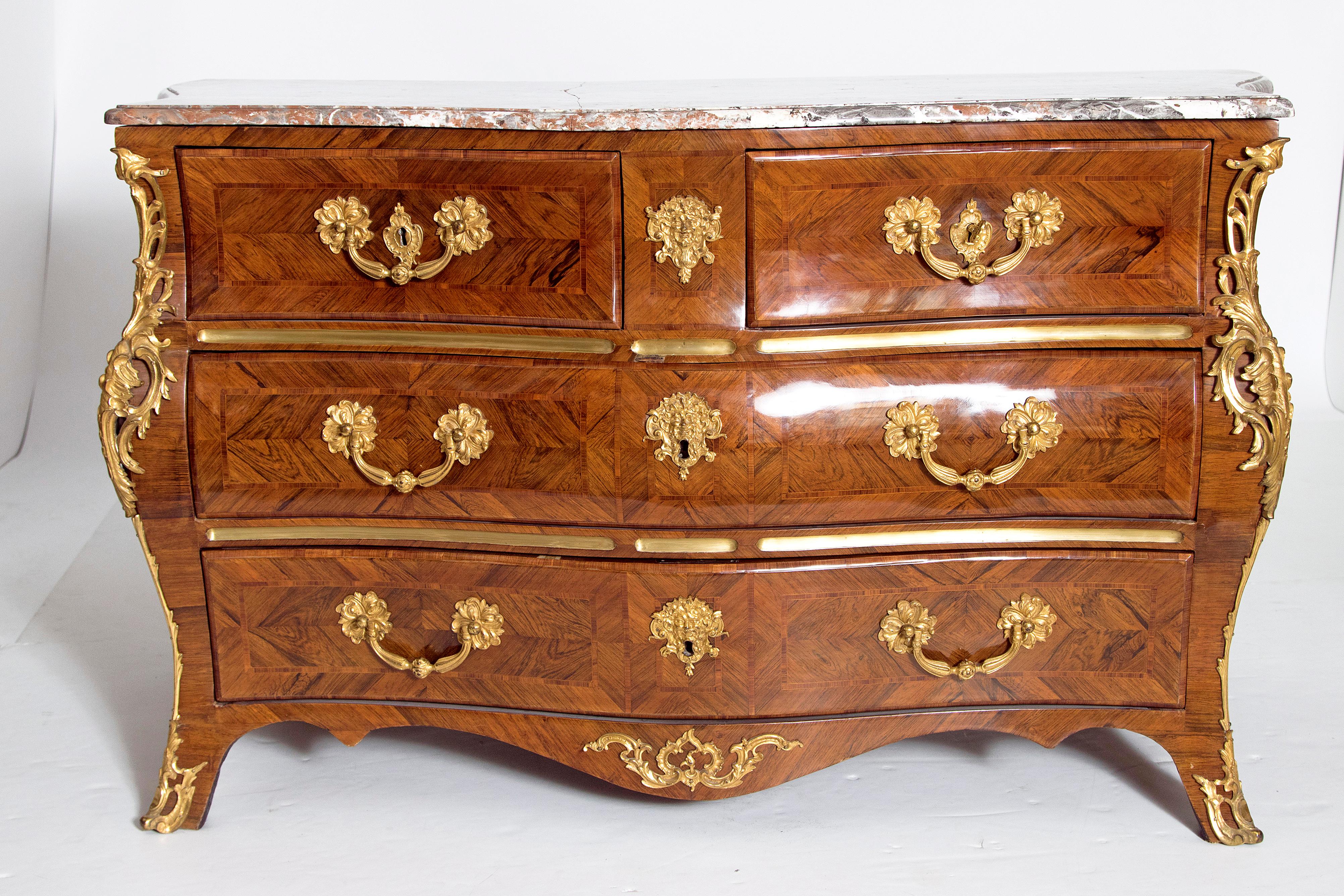A handsome French Regence bombe four-drawer commode with dore bronze hardware, escutcheons, and trim. Two small drawers above two large drawers with key. Drawer fronts have intricate herringbone inlay all around. The inlay continues on two panels on