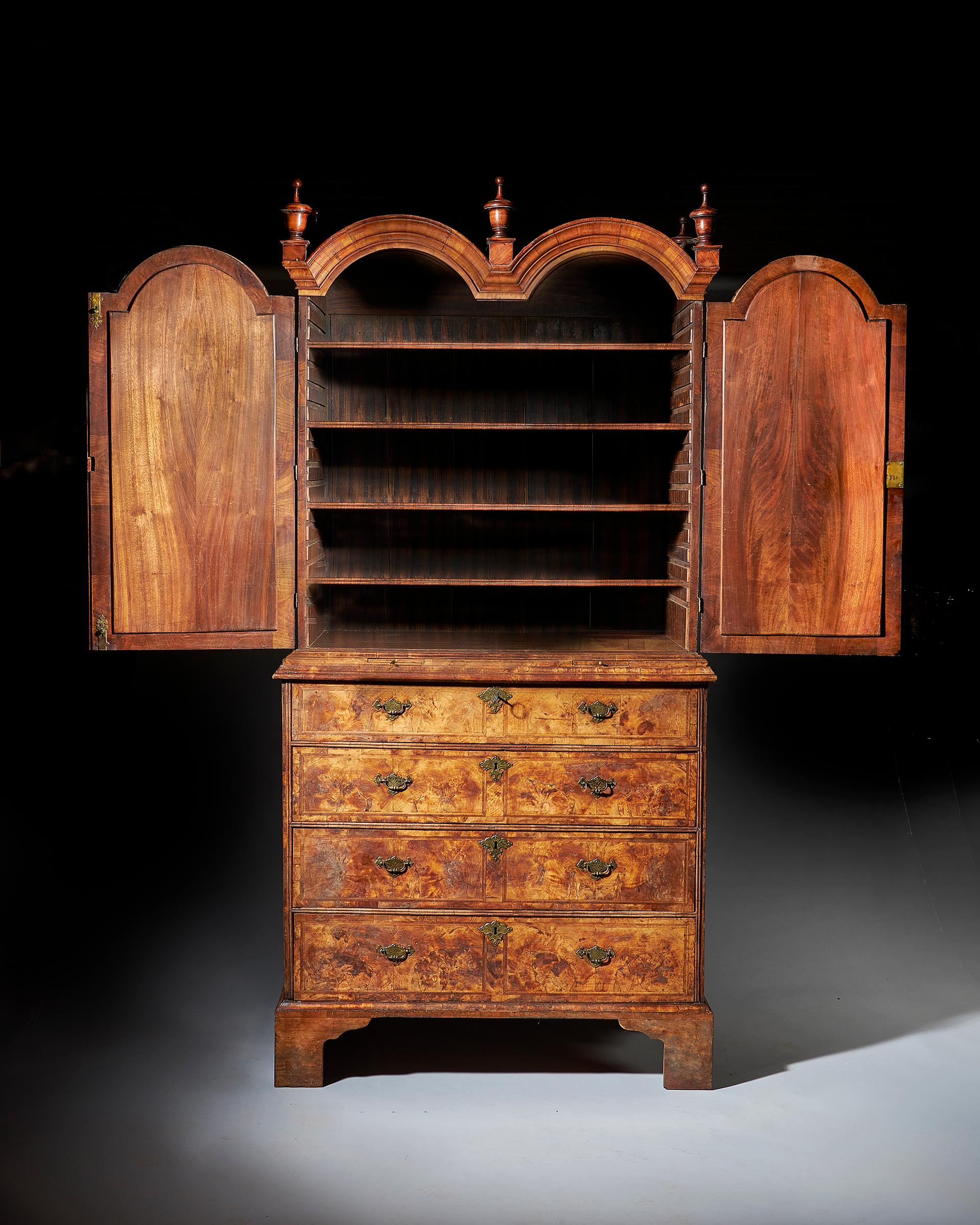 An exceptional and original highly figured George I walnut double dome bookcase on chest, circa 1720-1730.

To the bookcase, original surmounted walnut finials on moulded chimneys sit above well-shaped moulded double dome arches to the front and
