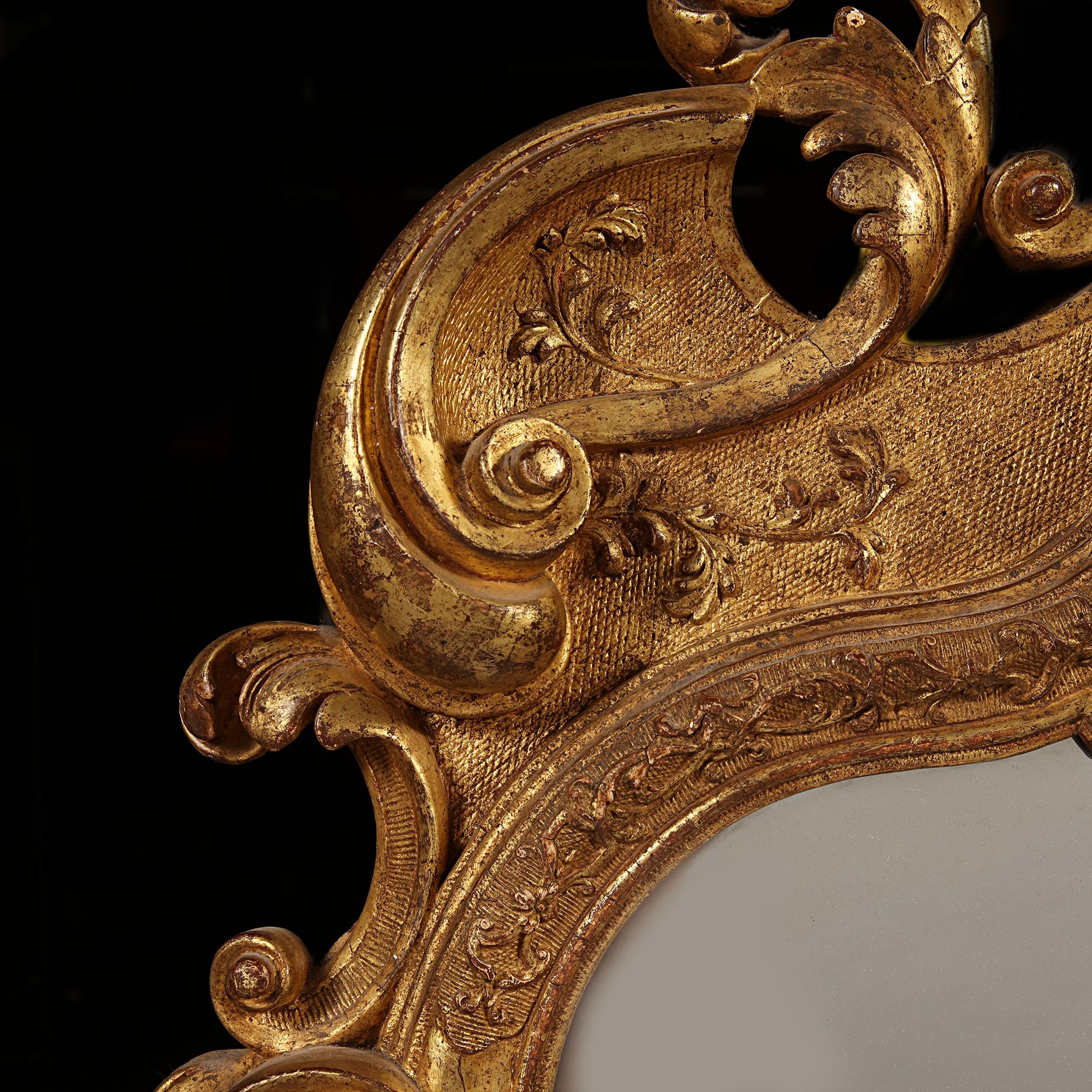 A fine early 18th century German giltwood pier mirror, the gilt frame with burnished and hatched reserves in carved gesso overlaid with strapwork, the crest with a flamboyant arrangement of bold scrolls and acanthus ornament around a framed scallop