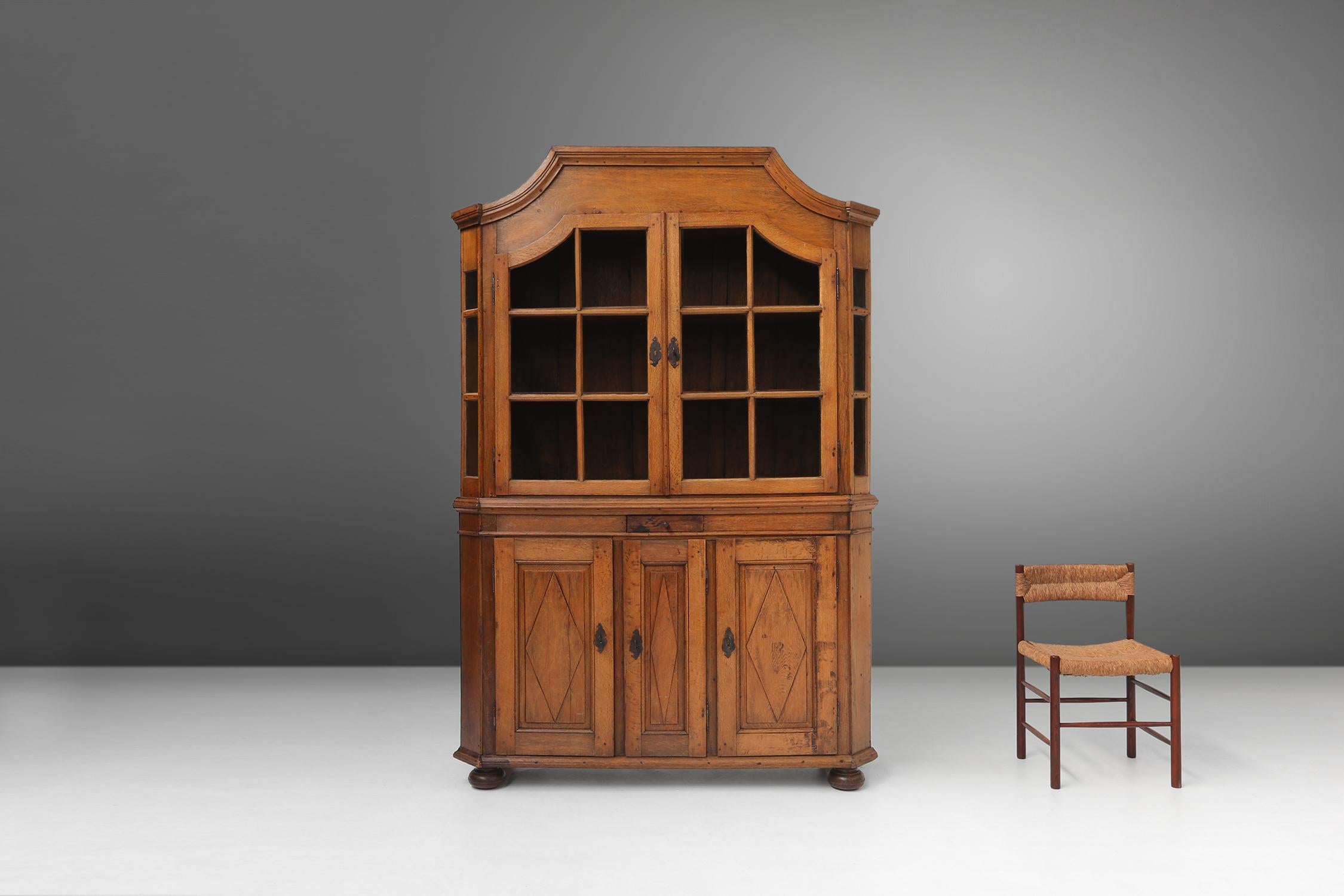Authentic 18th-century German display cabinet, a masterpiece of craftsmanship and design. Made of solid oak, this cabinet has a rich history and beauty. You can see the authenticity by the original blown glass, which is a rare and precious feature.