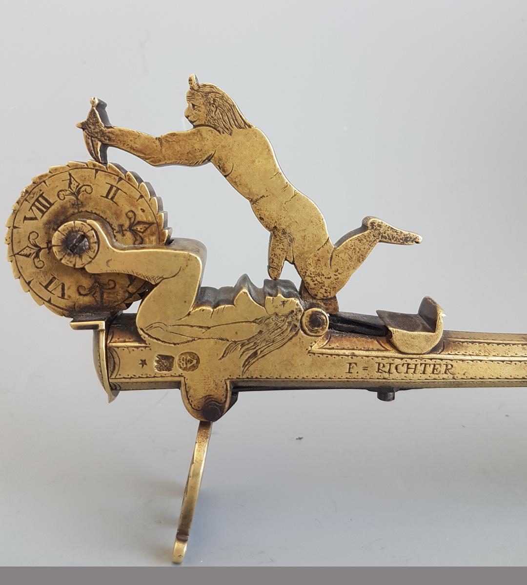 A superb and very rare early 18th brass and mahogany pistol handled gunpowder tester, signed 'F. Richter', modelled and engraved with an erotic scene of a naked devil and woman. Stamped on the other side 