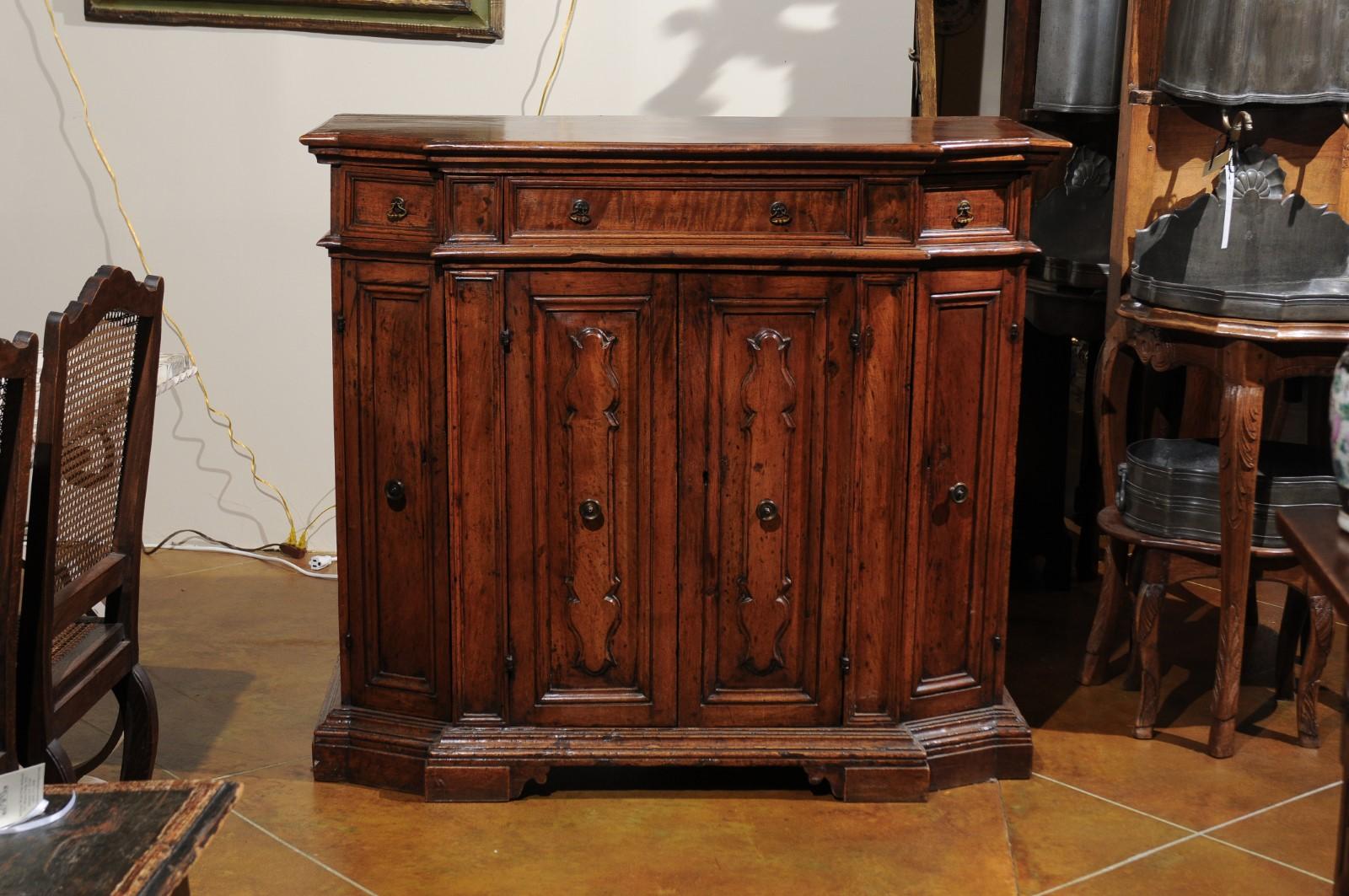 An early 18th century Italian Baroque walnut credenza with 3 drawers, 4 cabinet doors with raised panels ending in carved bracket feet.