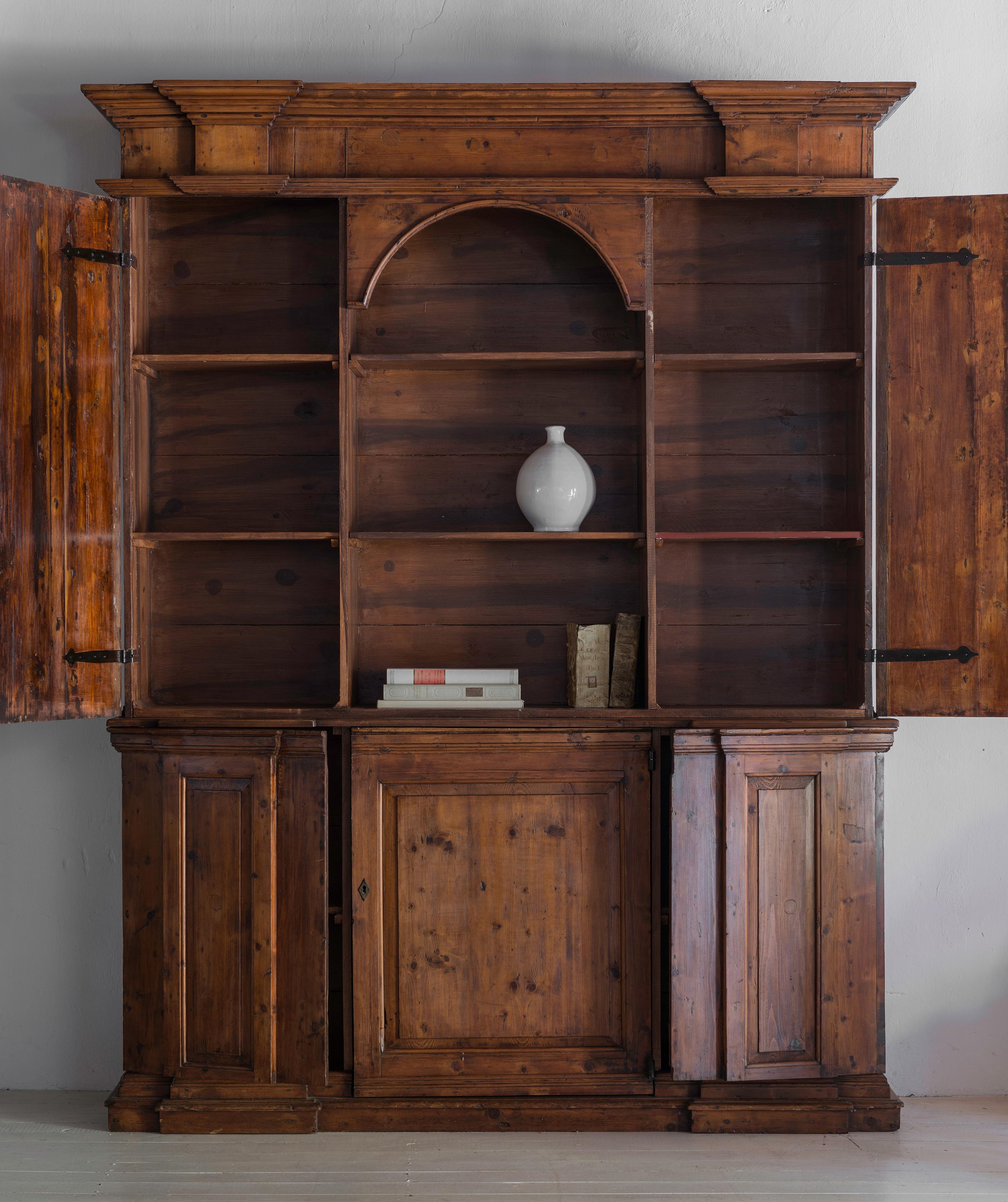 Un'imponente libreria o buffet scultoreo a due corpi, Toscana o Umbria, inizio XVIII secolo, con una bella patina calda. 

La parte superiore presenta porte pannellate su entrambi i lati accentuate da lesene ioniche e un vano centrale aperto con