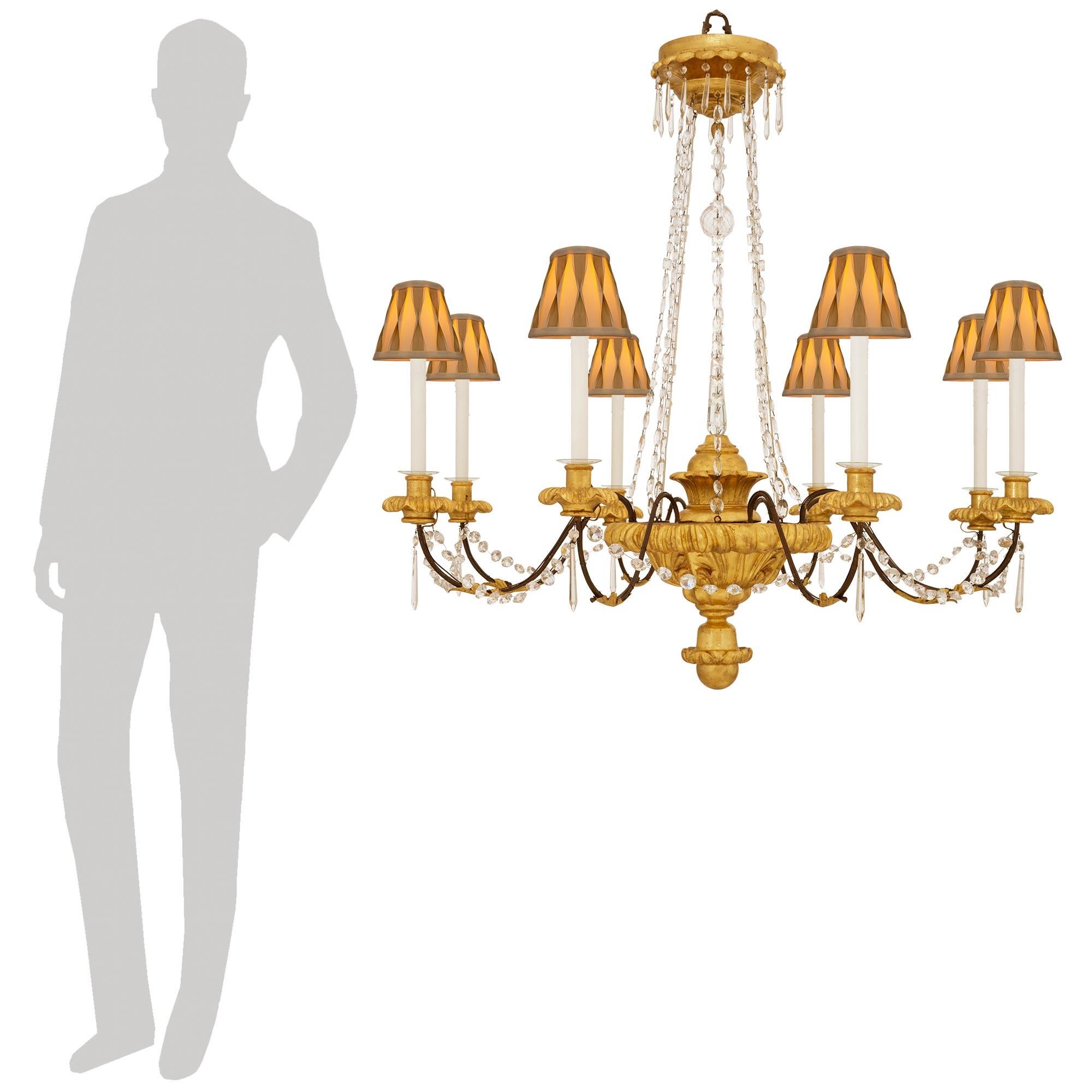 Un lampadario decorativo ed elegante del periodo Luigi Barocco del XVIII secolo in legno dorato, ferro e cristallo. Questo imponente lampadario a otto bracci è centrato in basso da un meraviglioso terminale a sfera in legno d'orato con una fascia