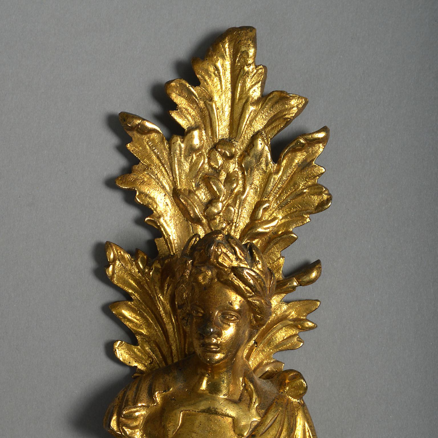 The gilt brass backplates formed of tapering pedestals surmounted by opposing busts with foliate surrounds and supporting two candle-branches.