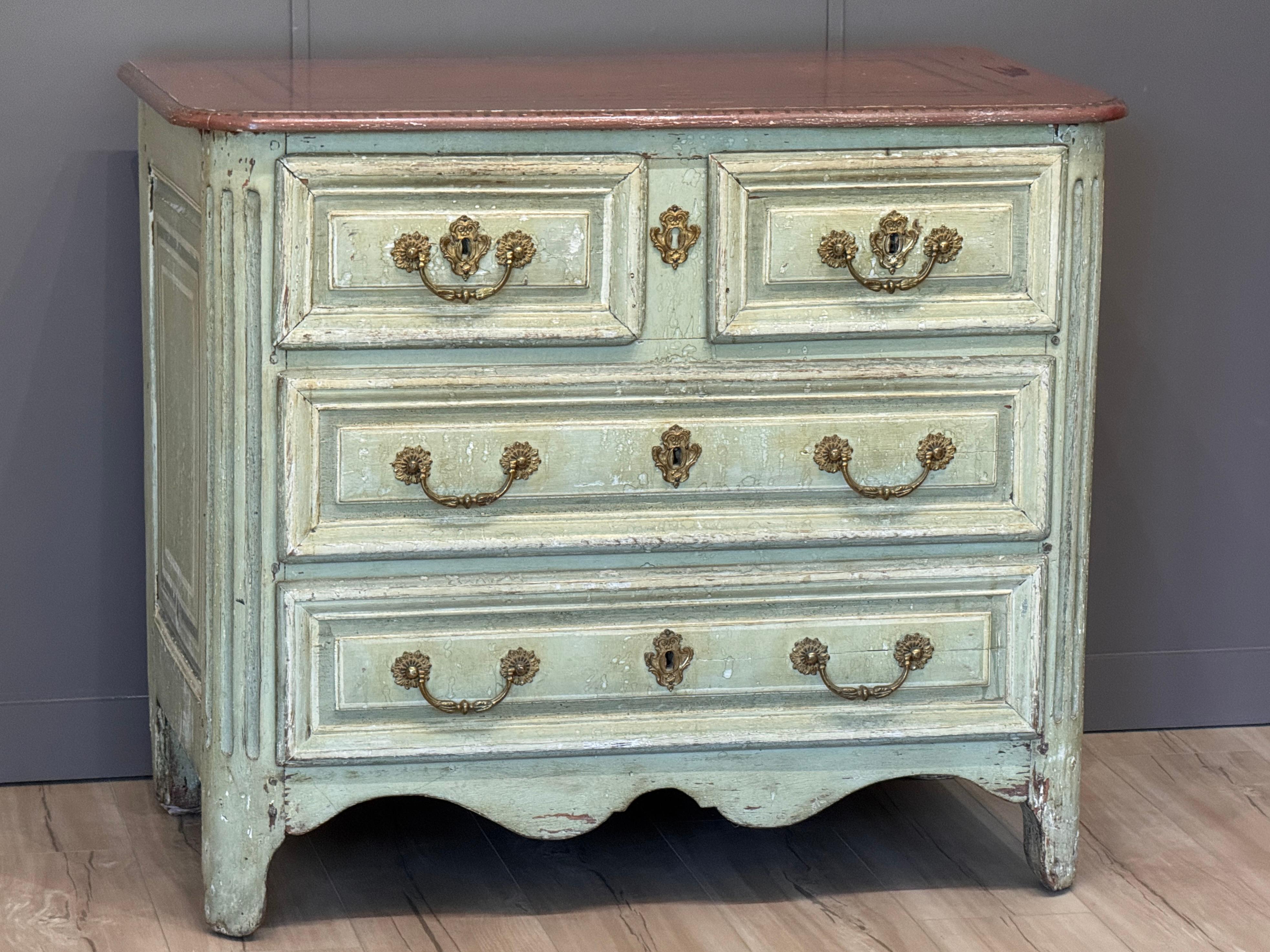 An early 18th century French Louis XV provincial commode, retaining a charming original painted surface in soft green with a contrasting painted top. The shaped apron and fluted corners emphasize the curving lines of the period. Original hardware