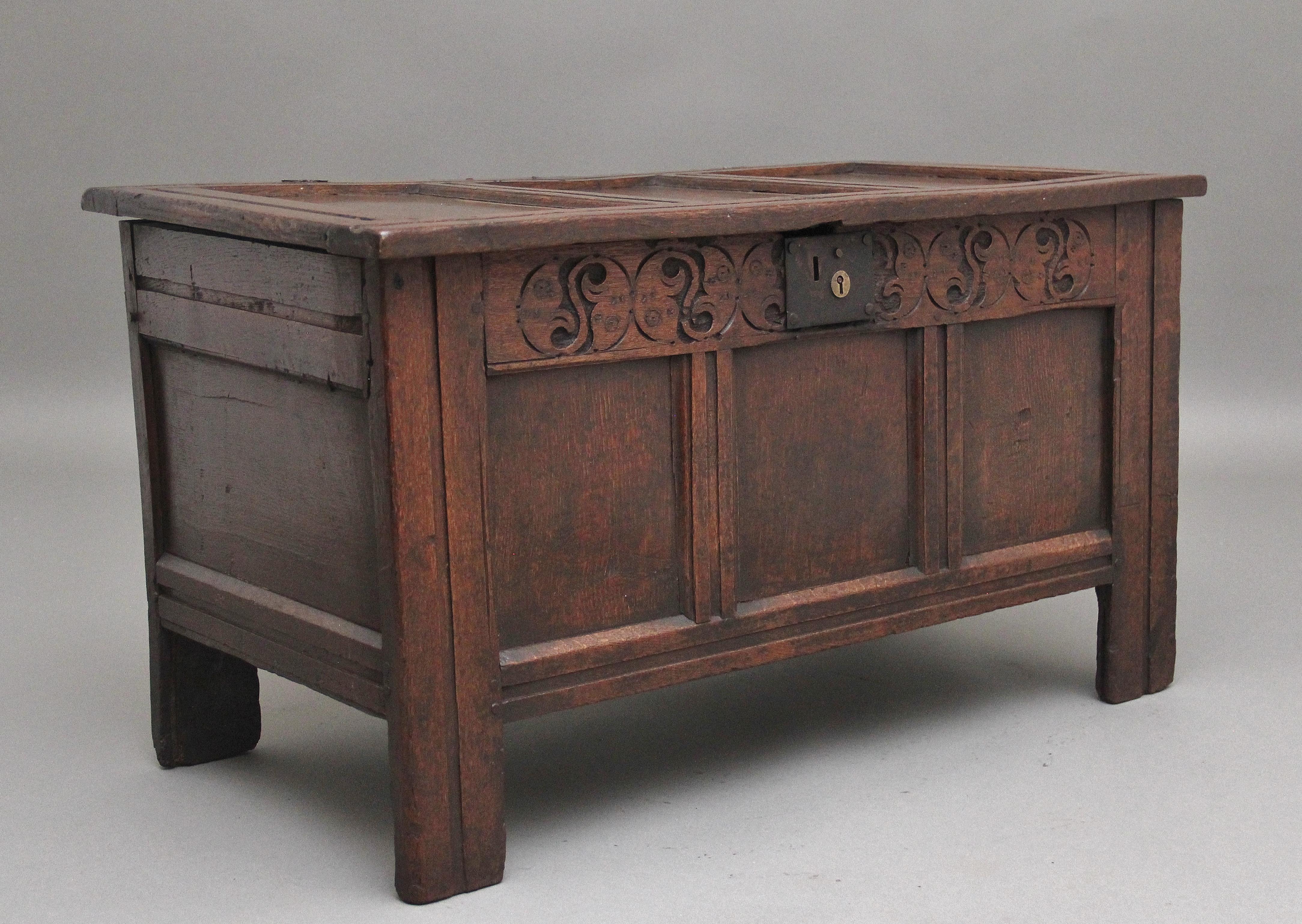 Early 18th Century oak coffer with the hinged three panelled top opening to reveal a large compartment space, the three panelled front having wonderful decorative carving, panelled sides, standing on square legs.  This coffer has a lovely warm oak