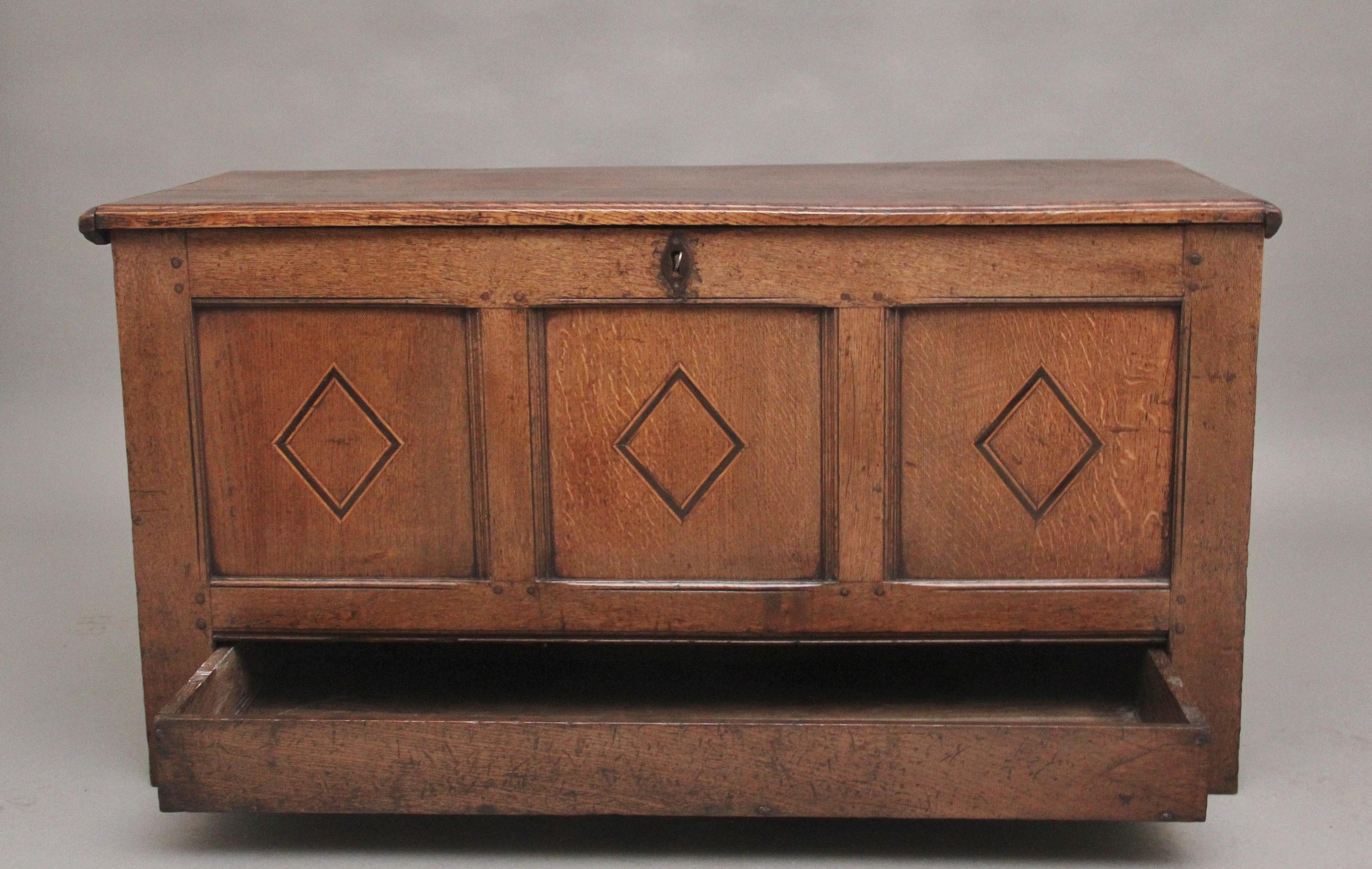 A nice quality early 18th Century oak coffer, the hinged moulded edge top lifting up to reveal a large compartment space and a candle box to the side, the three panelled front having decorative carving on each panel, and a long frieze drawer below