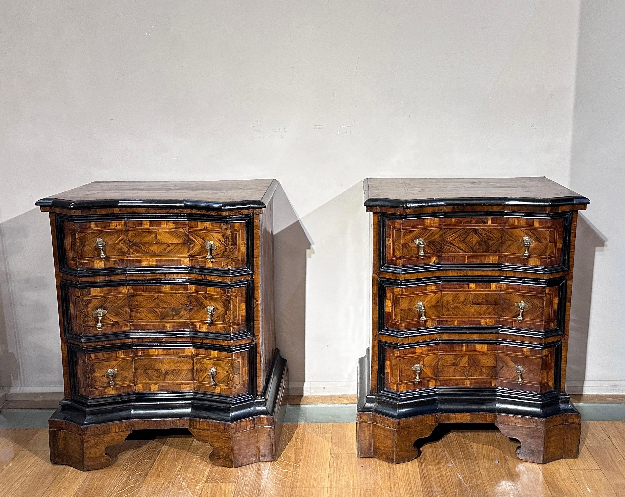 Elegant pair of walnut veneered chests of drawers with geometric motifs and ebonized wood finishes. The wavy front, the owl's beak shaped top and the shelf base give a unique elegance to these pieces of furniture. One of the two drawers has drawers,