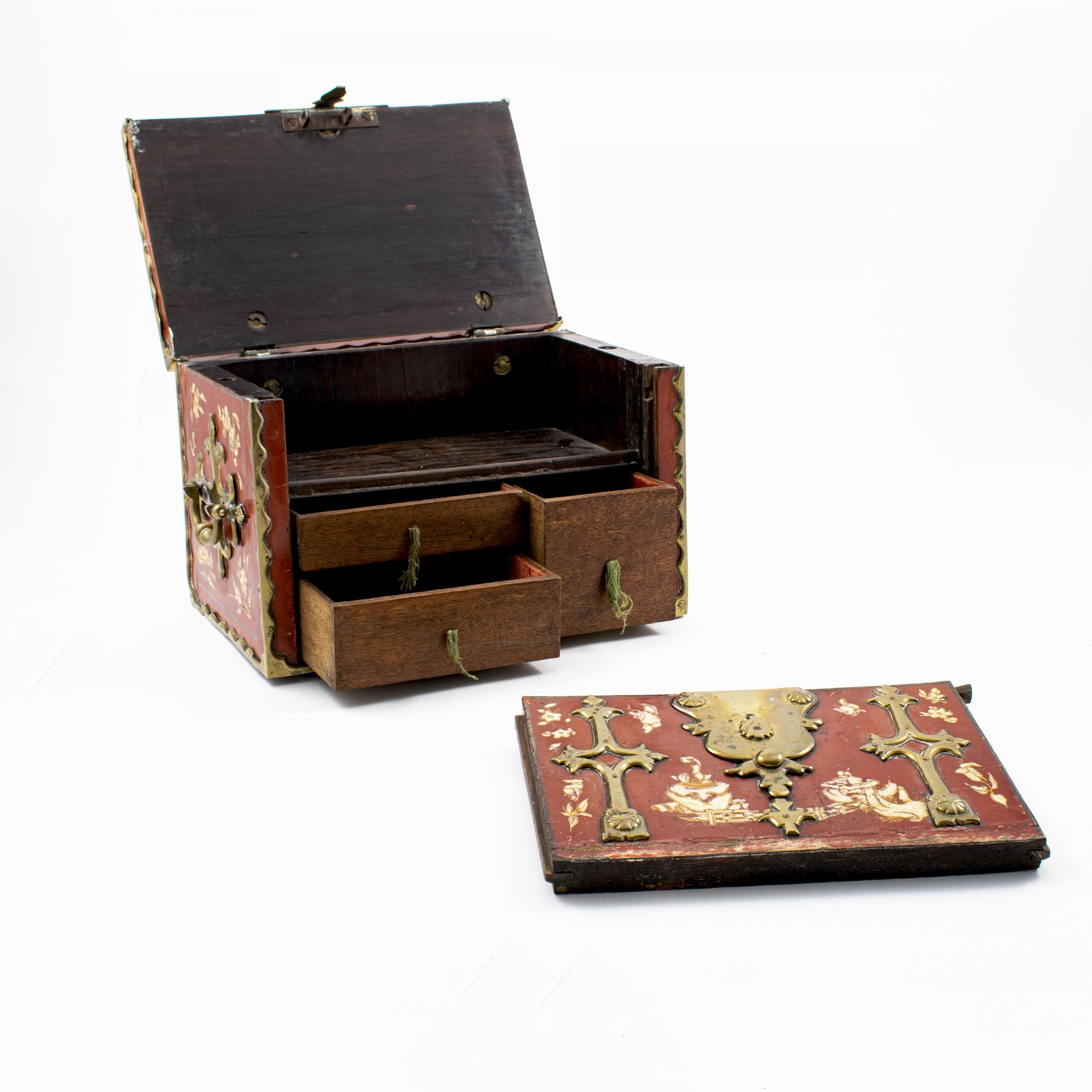 Rare Dutch baroque box composed of padauk wood with original red lacquer finish, decorated with ivory lacquer with gold outline. Richly adorned with heavy brass (or bronze) decorative mounts and two carrying handles on either side.
Under lid a lage