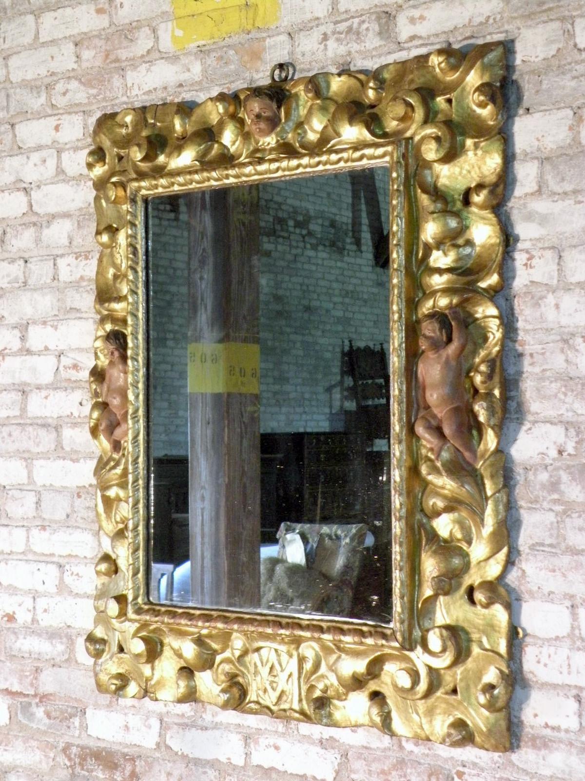A very decorative gilt wood mirror frame, adorned with painted putti to the left and right, a putti head to the center top and monogram initials 