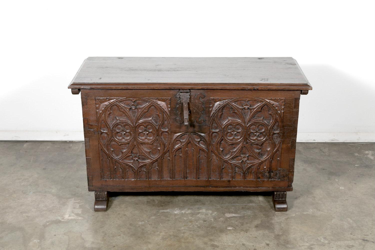 Intricately carved early-18th century Gothic style coffer handcrafted in Spain of solid oak. This small trunk, having its original hand wrought iron hardware, with a thick and solid carved lift top with beveled edges, and typical relief carved