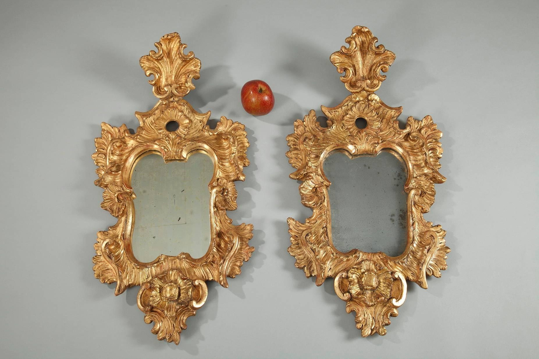 Early 18th century pair of Venetian wall mirrors. Each of them features an intricately carved giltwood frame crafted in the opulent Rococo style, with its foliate decoration of acanthus leaves, sweeping scrolls and shells. These small wooden mirrors