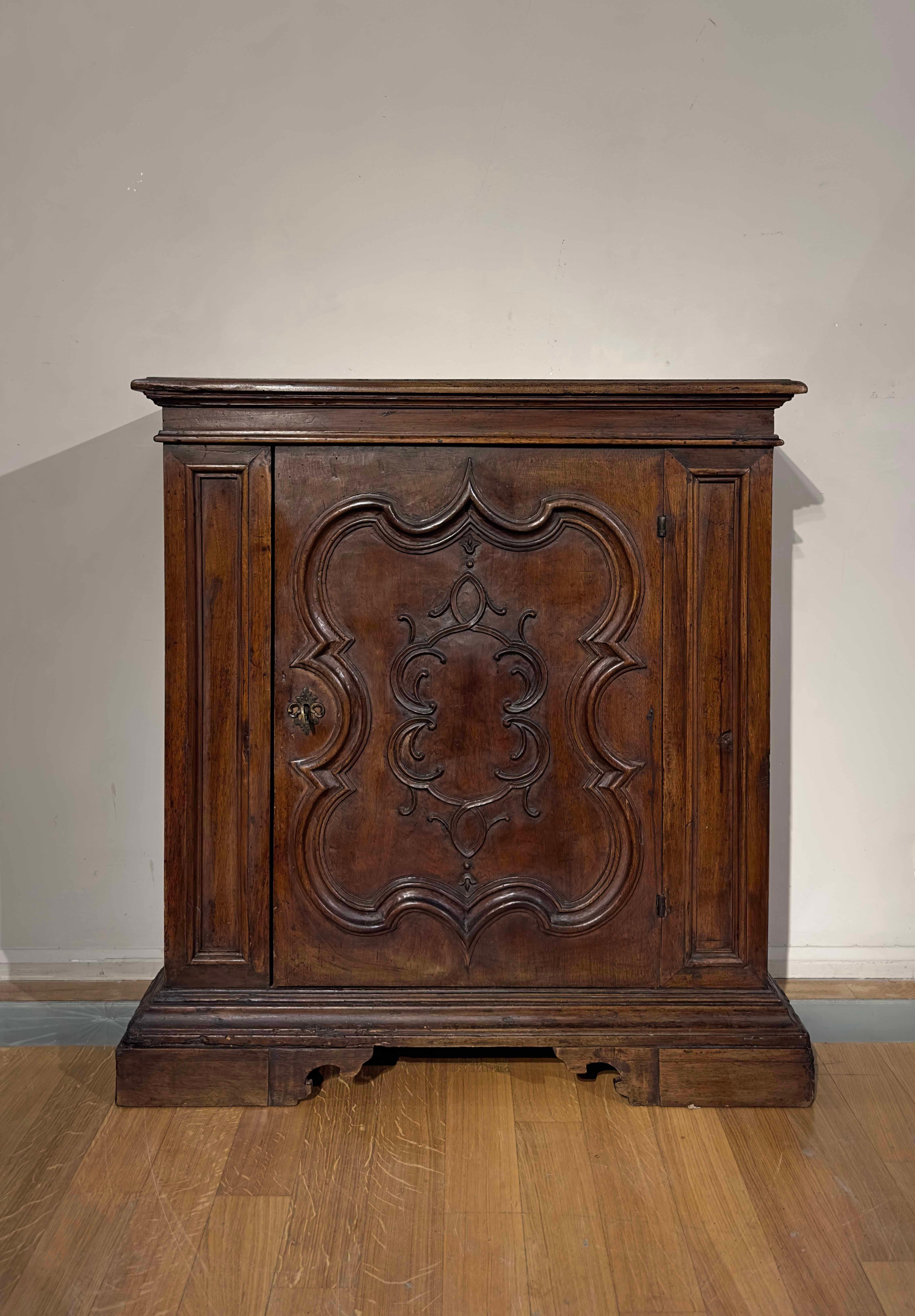 Beautiful Venetian small sideboard in solid walnut, with a smooth top and shelf feet. The peculiarity of this piece of furniture can be seen in the carving of the door, made by digging into the thickness of the door itself, creating decorative