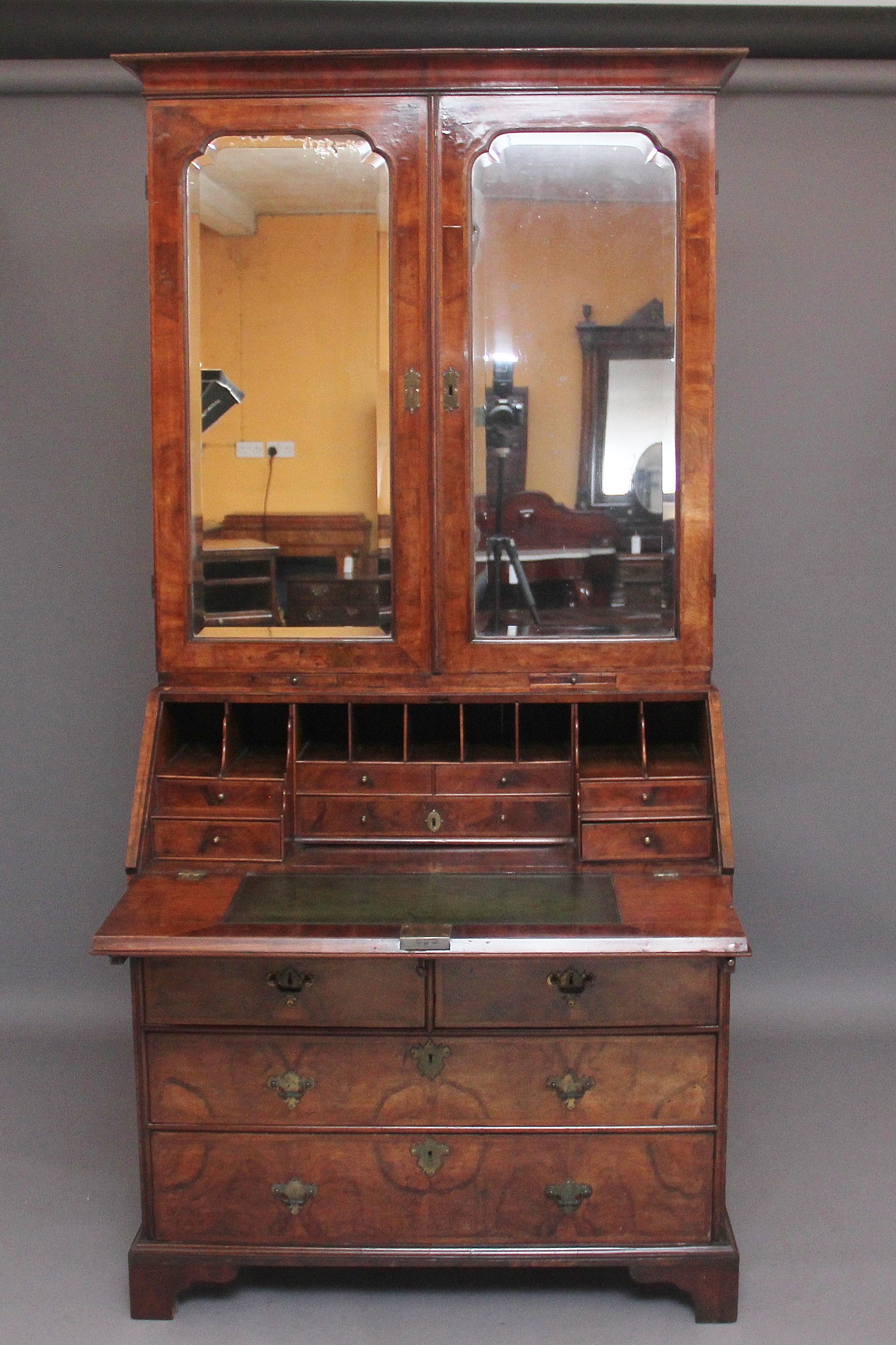 Early 18th century walnut bureau bookcase, the shaped cornice above a mirrored front bookcase with the two doors opening to reveal shelf space, various compartments and six oak lined drawers, the bottom of the bookcase having two pull out candle