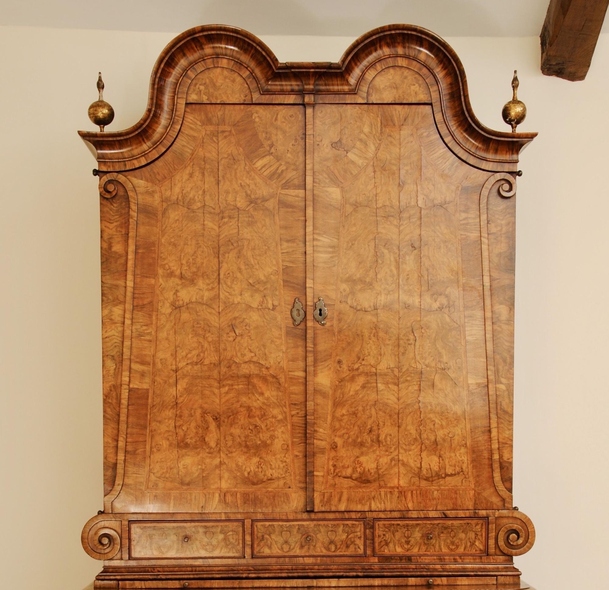 An early 18th century double dome burr walnut cabinet with an unusual scroll design to the sides of the doors creating the illusion of a tapering top section, the chest below with bomb shaped design and scroll feet.
This stunning piece retains the