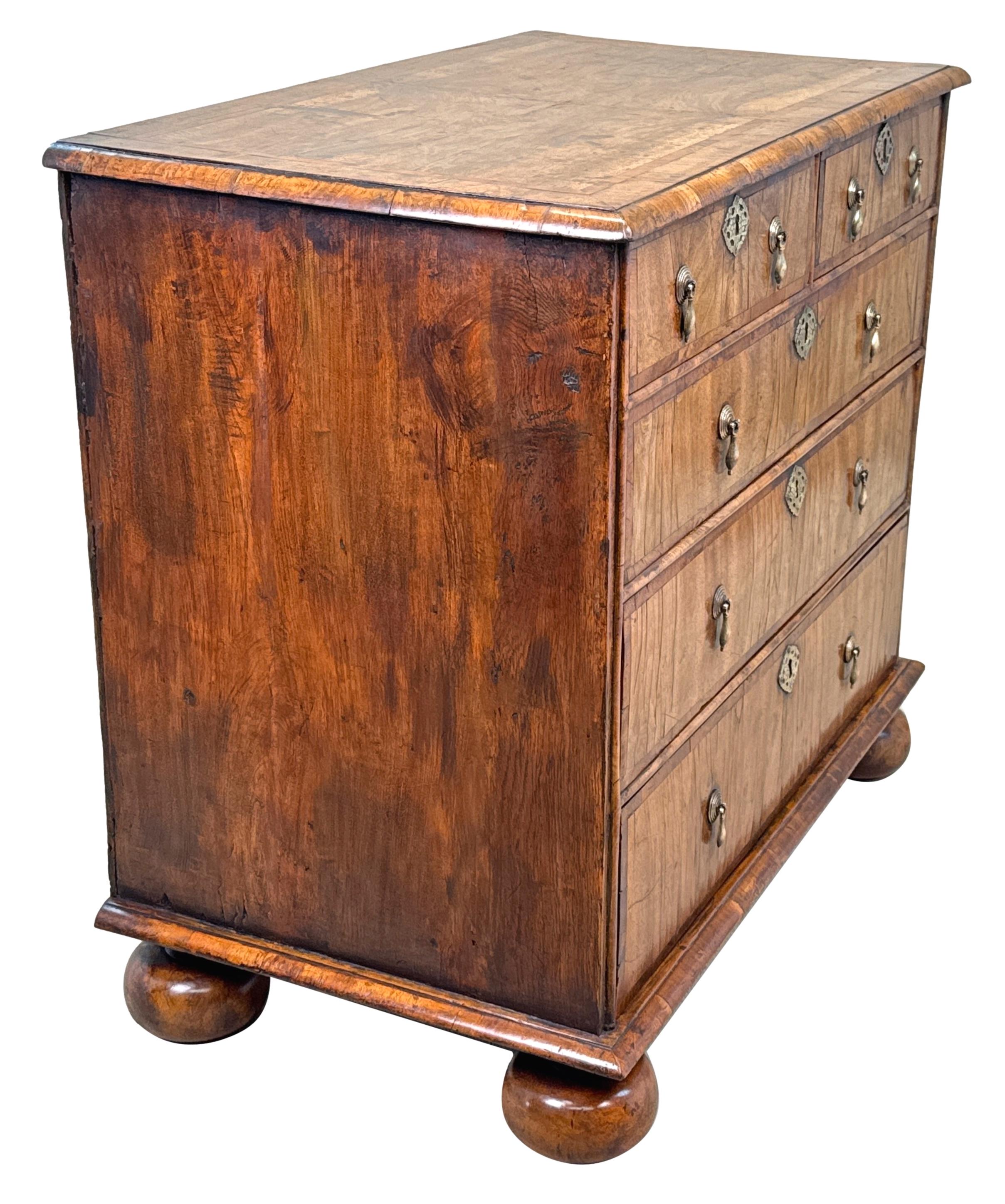 A Very Attractive And Charming Early 18th Century, Queen Anne Period, Walnut Chest Having Superbly Figured Quarter Veneered Top, With Elegant Banded Decoration, Over Two Short And Three Long Drawers, With Replacement Brasswear, Raised On Replacement