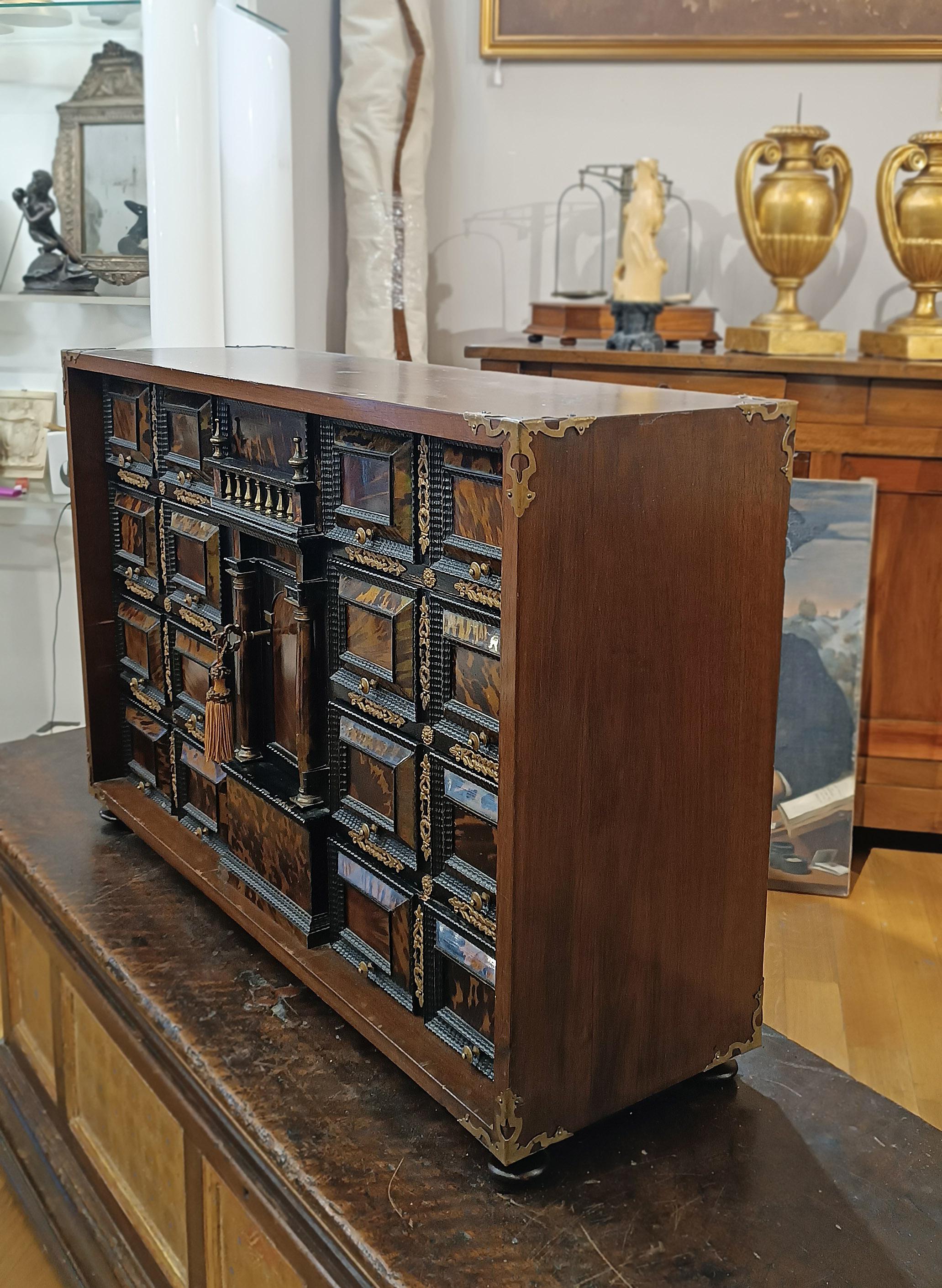 Elegant and refined walnut coin cabinet, enriched with gilded bronze and ebonized wood finishes. The onion-shaped feet are made of ebonized wood, while the corners are adorned with gilded bronze details, characterized by vegetal and geometric