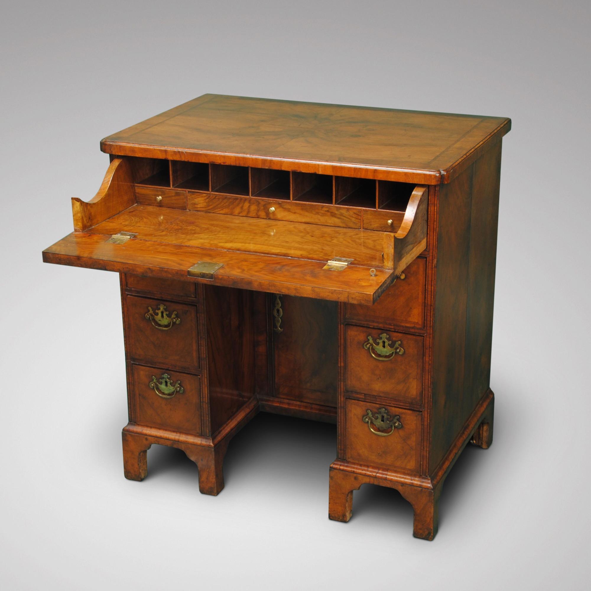 A walnut kneehole desk with quarter veneered top above an unusual fitted secretaire drawer. The kneehole with two banks of drawers all retaining the original brass handles.
  