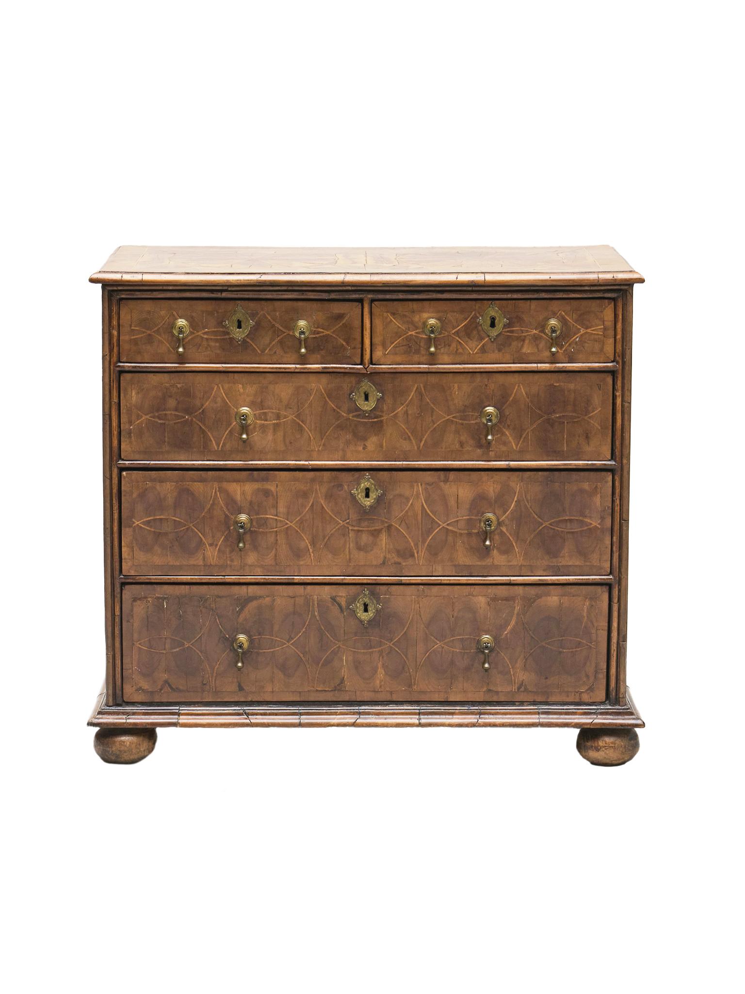 Fabriquée à la main au début du XVIIIe siècle, cette commode William & Mary est composée d'olivier et de noyer avec des ferrures en laiton. Des incrustations disposées selon un élégant motif concentrique ornent la façade des tiroirs, tandis que des