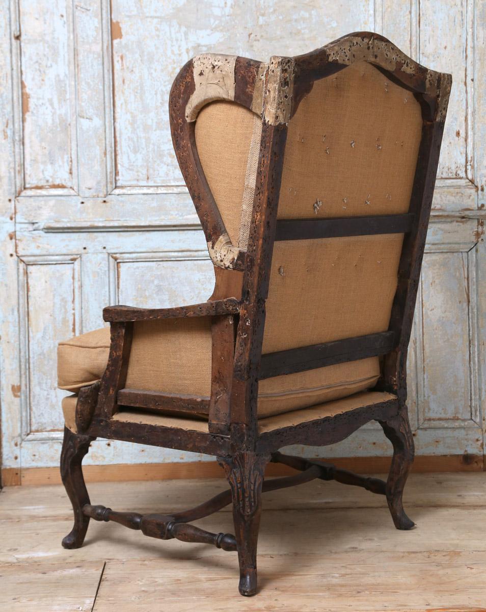 Early 19th French wingback chair constructed in mixed fruit woods giving a distressed finish the frame has been accented with nail tacks showing the true sole of the chair with later upholstery. The chair has a very strong presence and a great asset