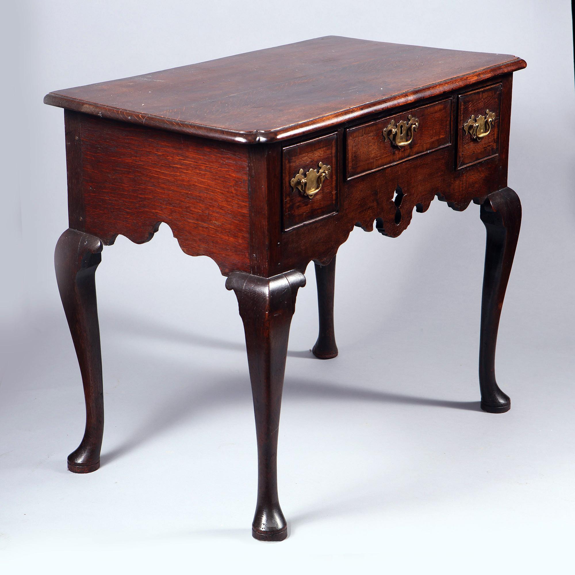 A fine early 18th century George I oak lowboy, the top with thumb molding and inswept corners above a bank of three drawers retaining their original brass hardware and iron locks, above and shaped pierced apron and raised on cabriole legs with pad