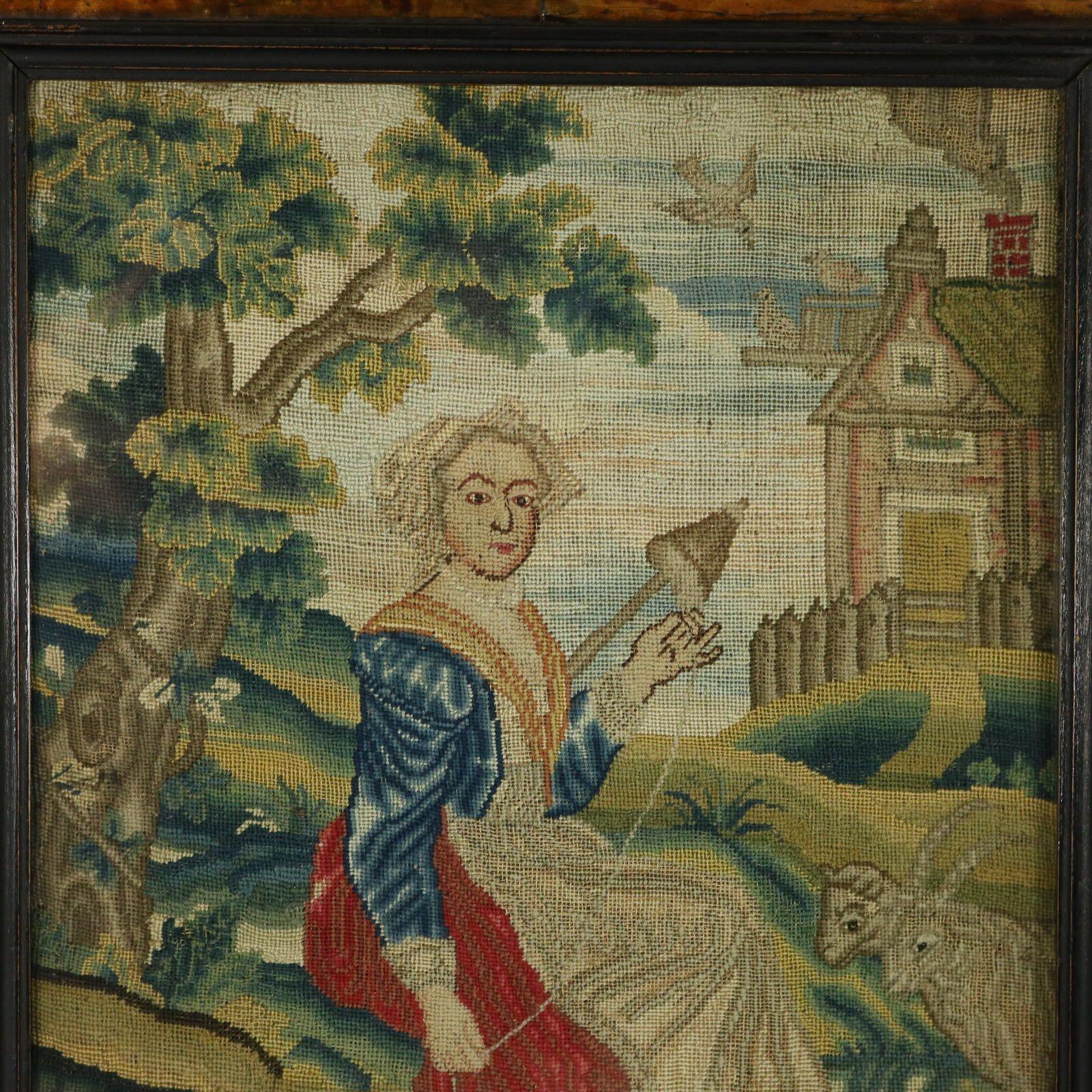 An 18th Century petit point silkwork embroidery of a lady seated next to a tree, in a country landscape. Goats, a dog and sheep in the foreground. A house in the background with a smoking chimney and birds perched on the roof. The piece is worked in