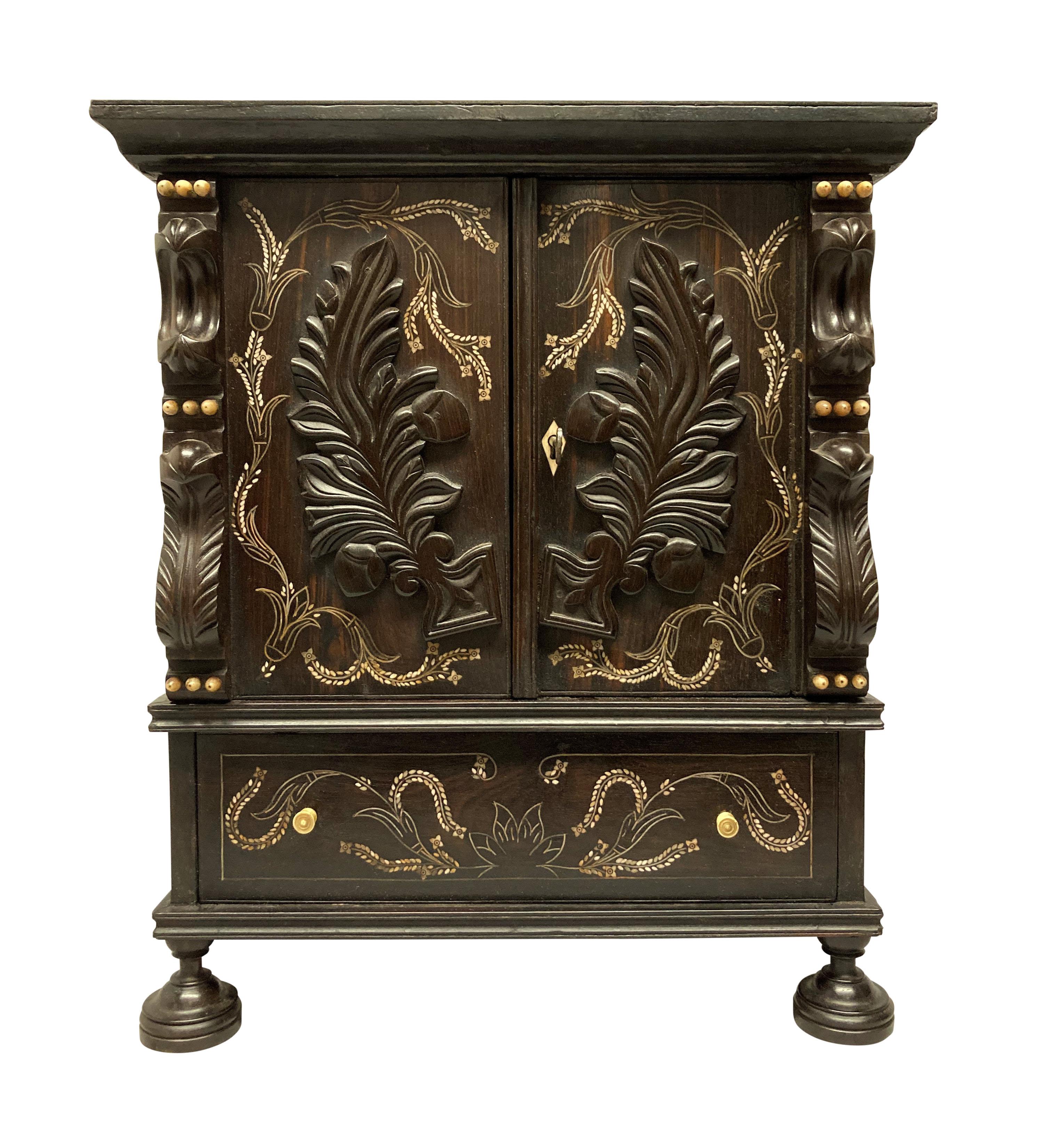 An unusual and beautifully carved Anglo-Indian small cabinet, with a fitted interior, lined in velvet and a fall front hidden cupboard. Carved from solid ebony and inlaid throughtout in bone.