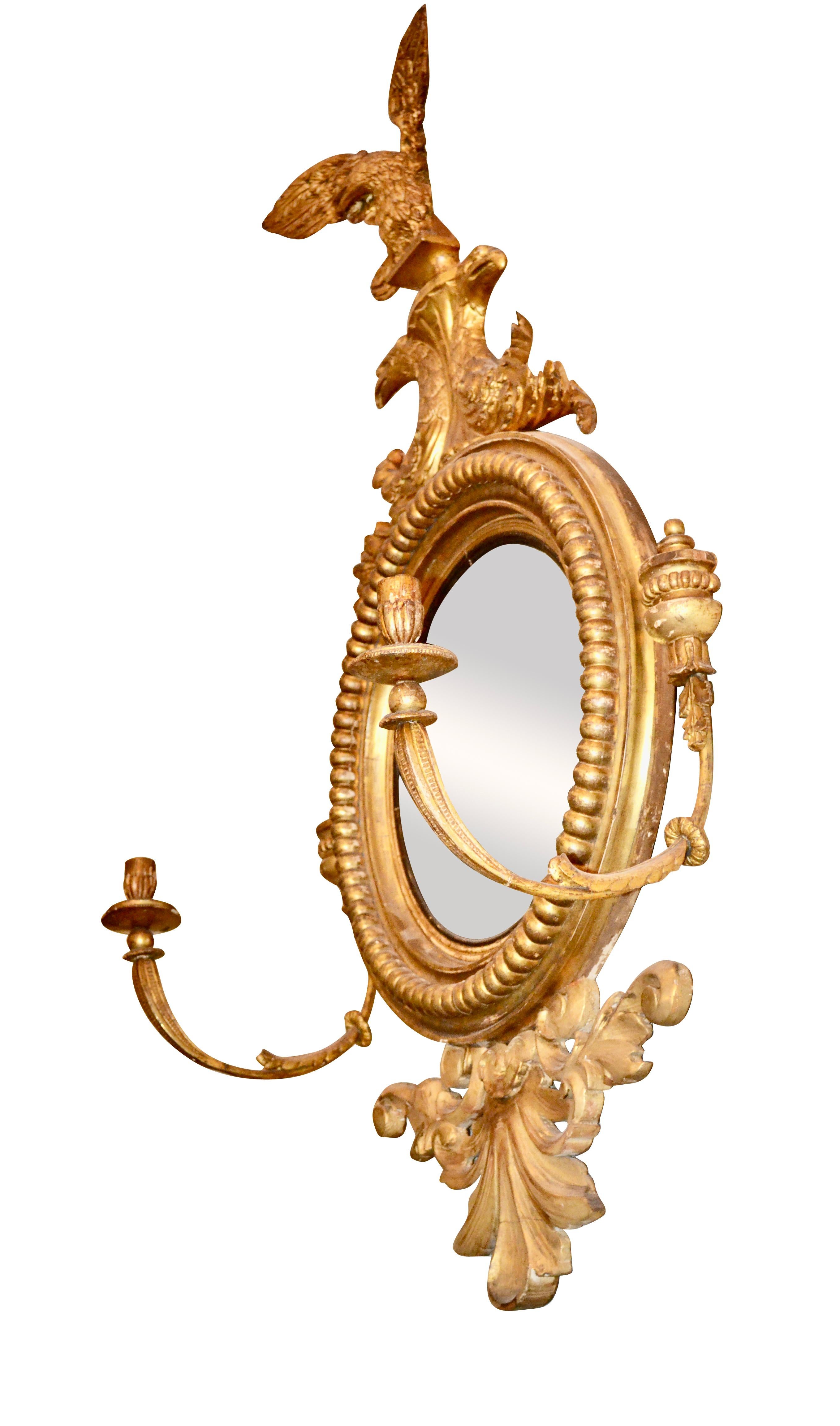 A period English Regency convex mirror in a carved and water gilt frame, the mirror is surmounted with two scrolling eagles heads which support a third complete eagle with its wings fully spread. The mirror has a carved decorative element on the