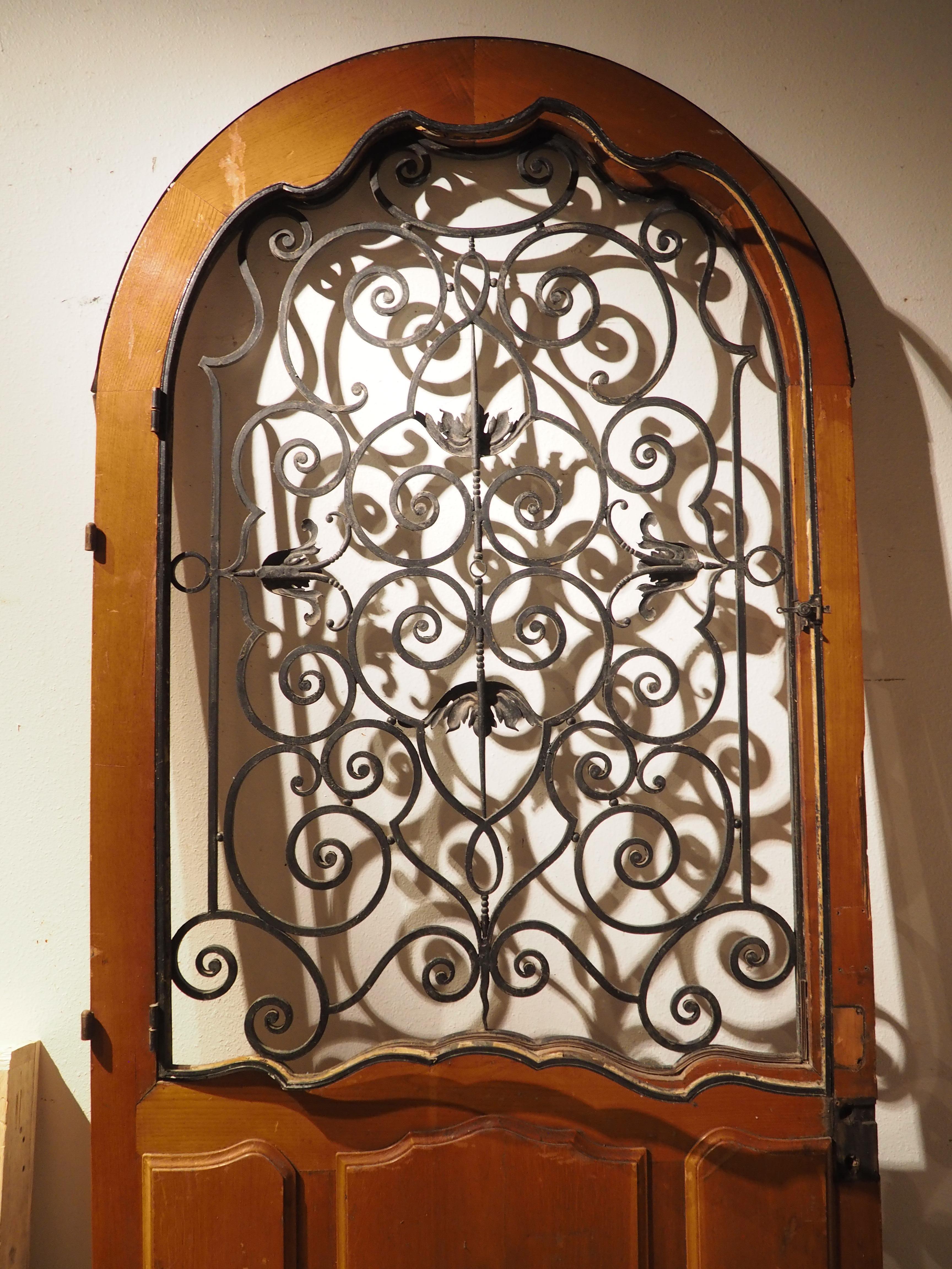 This large entry door was found in the South of France and was constructed from oak, iron, and originally, glass. It has a pleasing arched top with a beautifully carved upper frame and lower section, while the upper half consists of shaped wrought