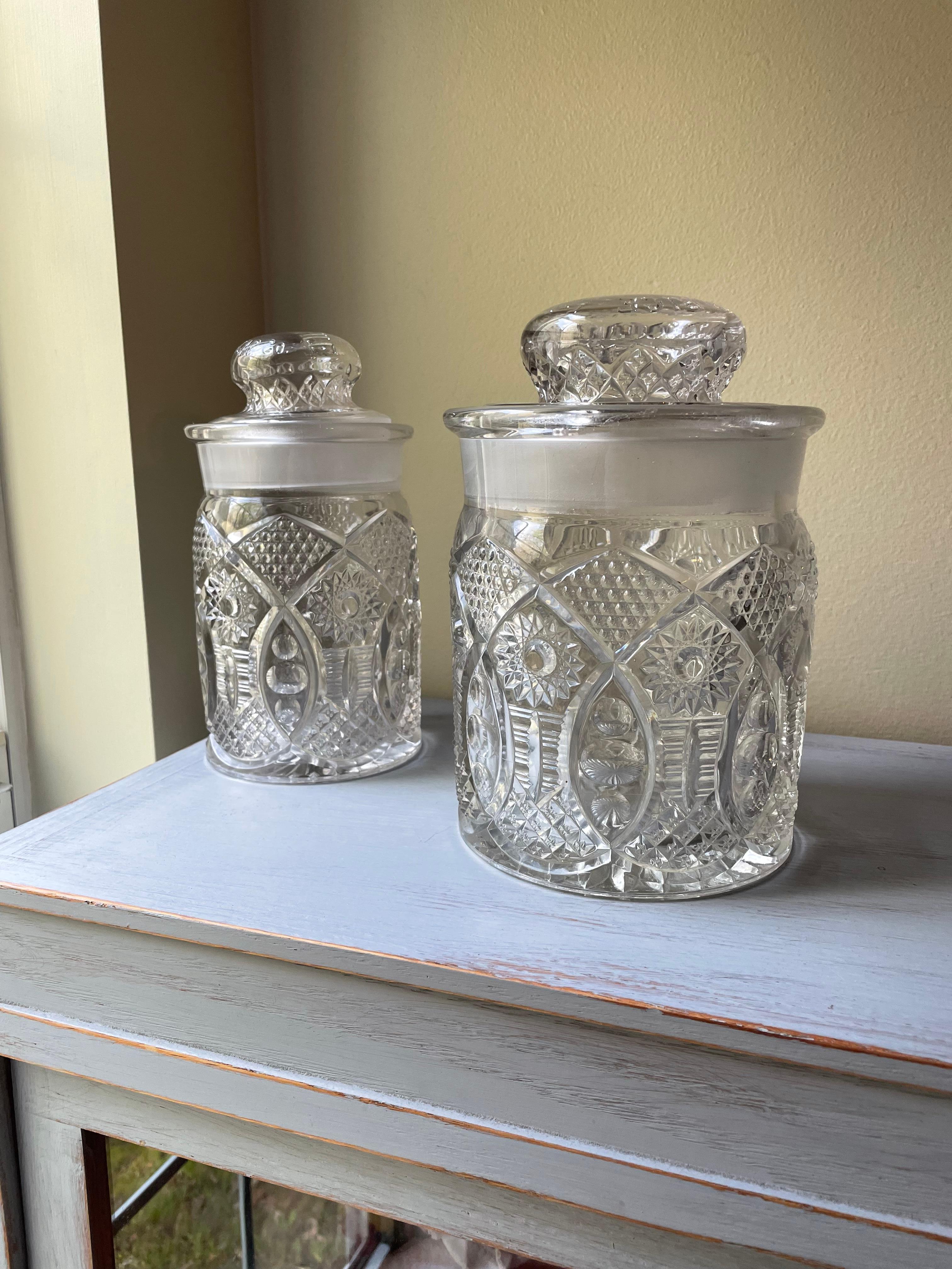 Antique pair of pressed glass humidors by F.C. Rice Mercantile Cigar Co. with their lids. This set has two different sized humidor jars. Both are in good condition considering their age and that they are glass. Both jars are in very good condition.