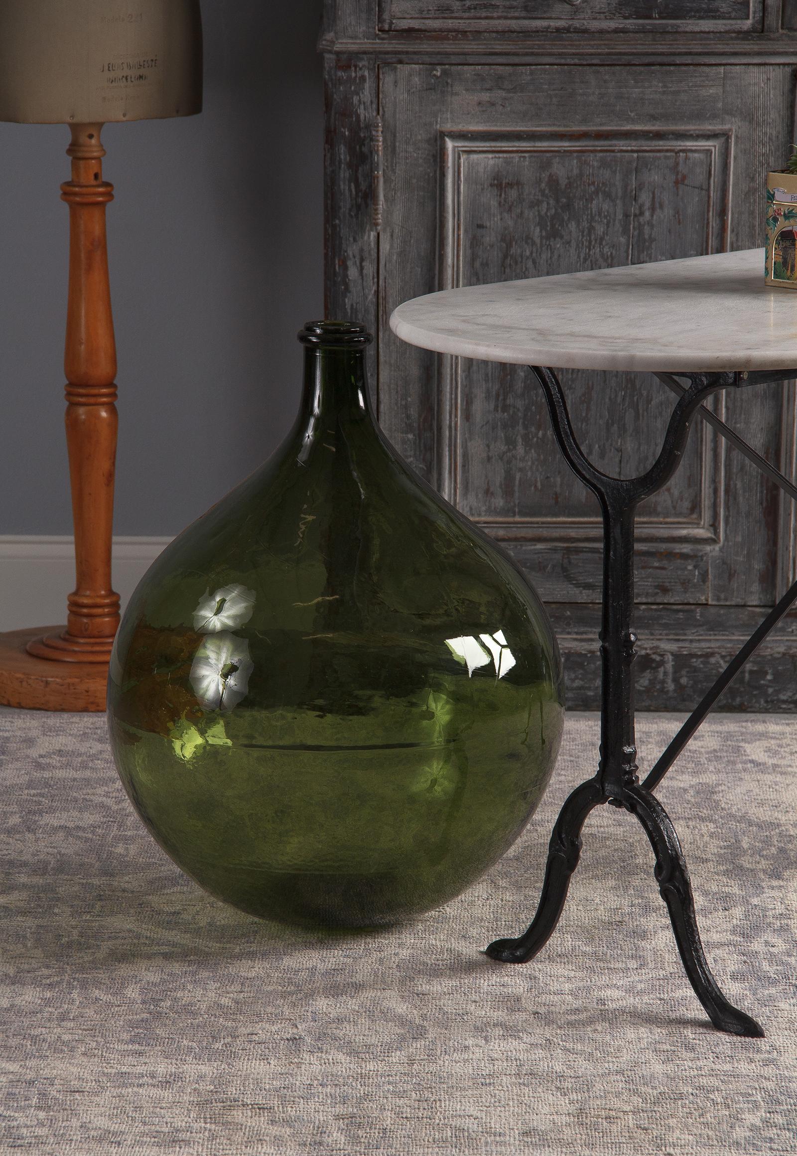 An oversized green glass bonbonne demijohn bottle, circa 1920. Wonderful green hand-blown glass was pressed into a mold and retains its ripples and bubbles. The mouth is 1.75