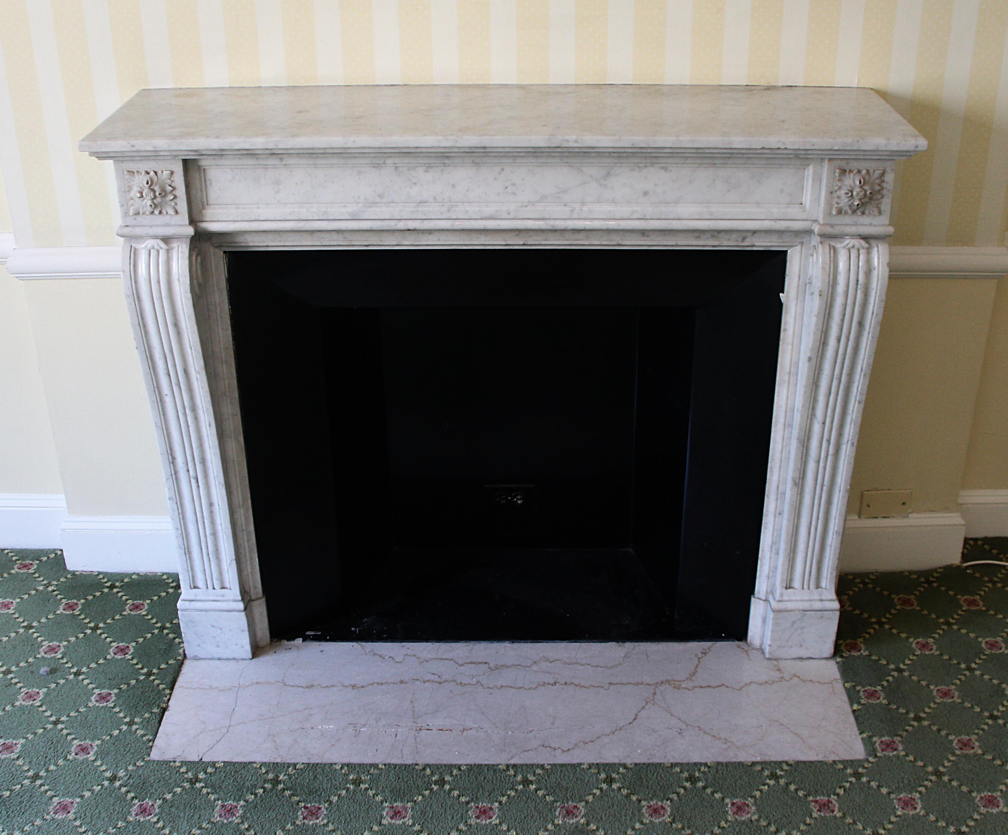 Louis XVI Regency Carrara white and gray marble mantel with rosette detail on the upper corners. Also fluted legs with slight protrusion at the top and scroll on the side. This was imported from France and installed in the Waldorf Astoria hotel in